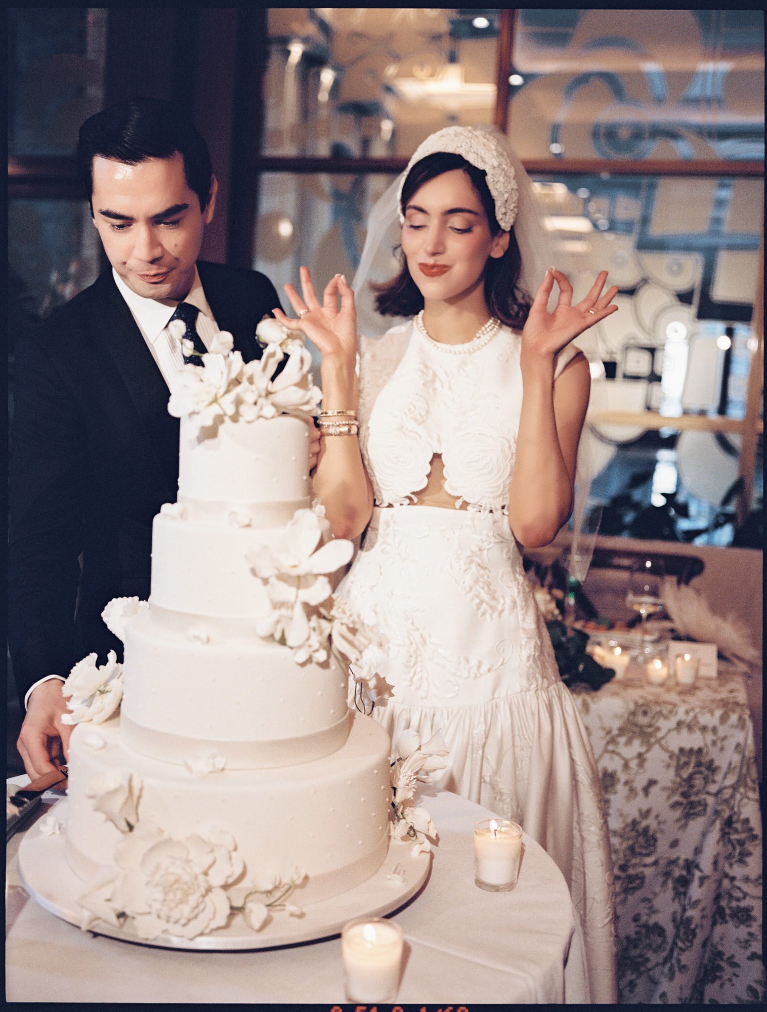 Bride laughing with her hands raised beside the groom and their four-tier wedding cake by Ron Ben Israel at the Waldorf Astoria New York, photographed by Jenny Fu.