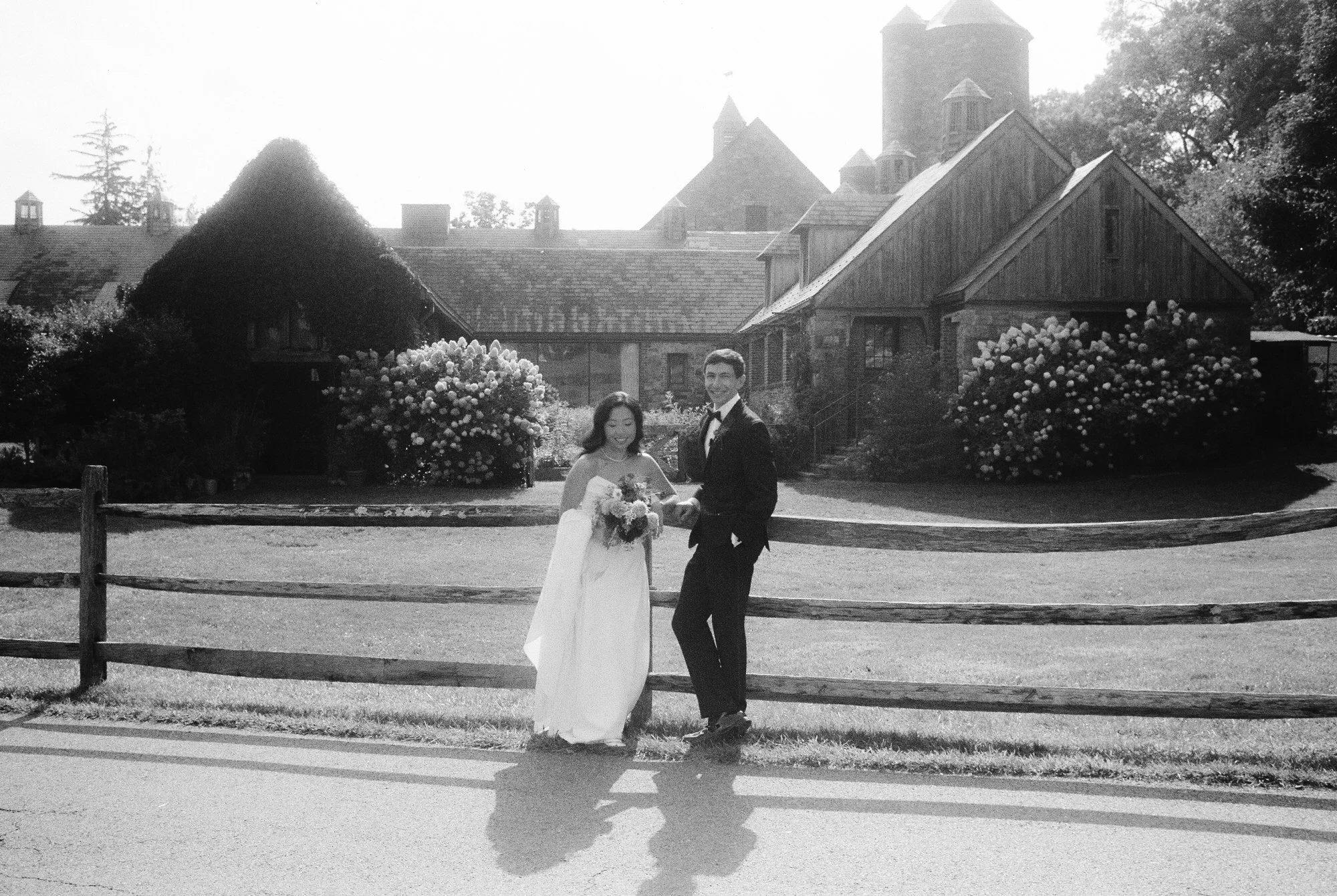 Bride and groom posing by the split rail fence with the stone barns behind them in black and white at Blue Hill at Stone Barns, photographed by Jenny Fu.