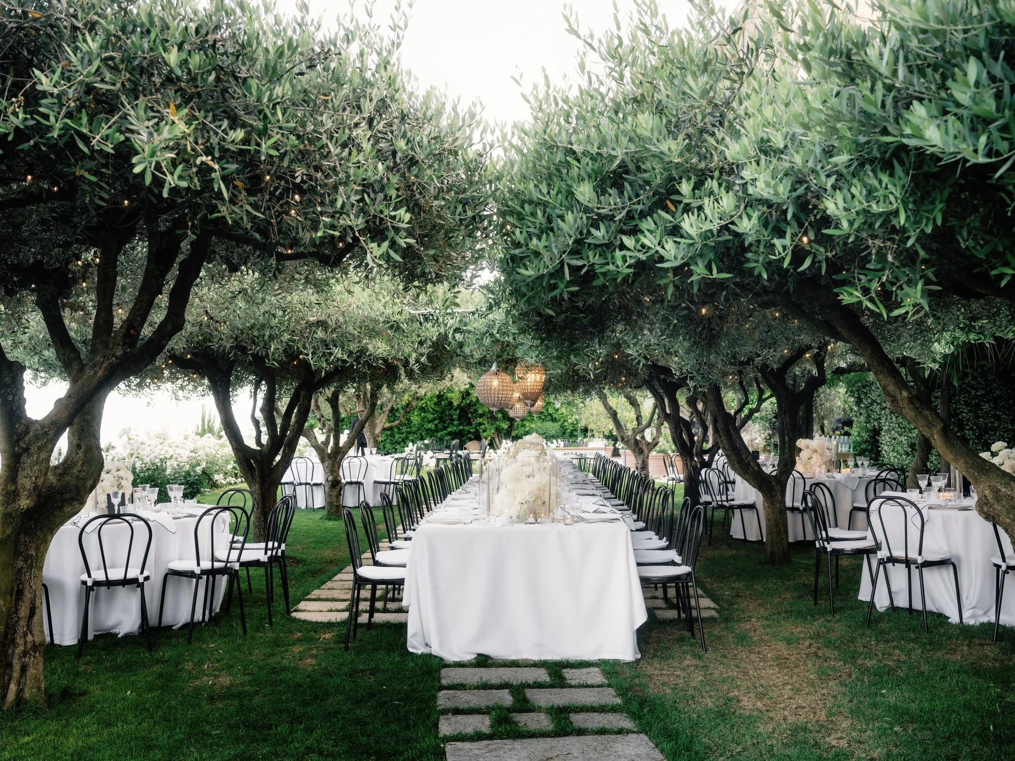 Candlelit dinner table adorned with white flowers and elegant place settings under olive trees at Caruso, A Belmond Hotel in Ravello, Italy, photographed by Jenny Fu.