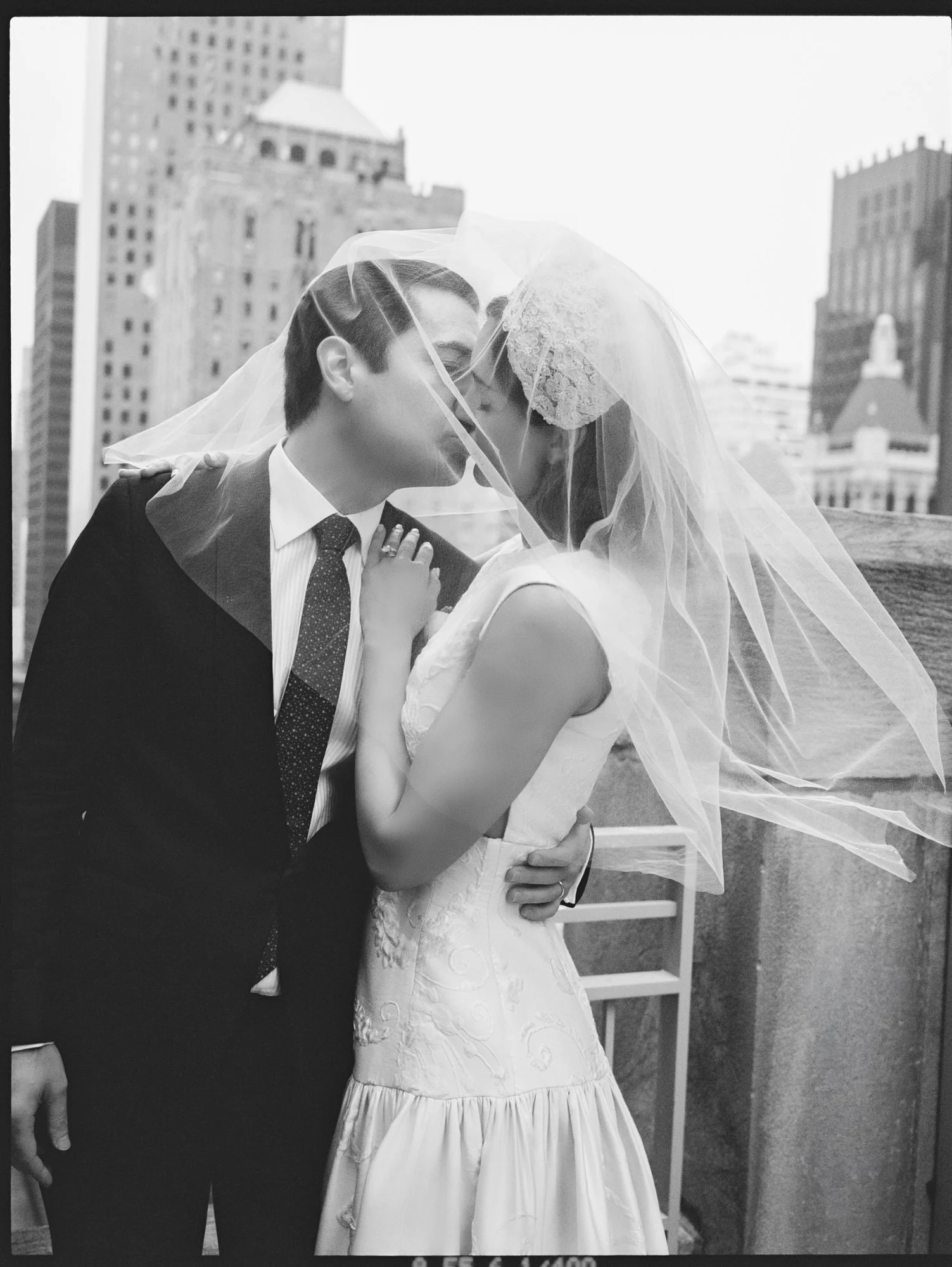 Black and white photo of the bride and groom kissing beneath her windswept veil with the Manhattan skyline behind them at the Waldorf Astoria New York, photographed by Jenny Fu.