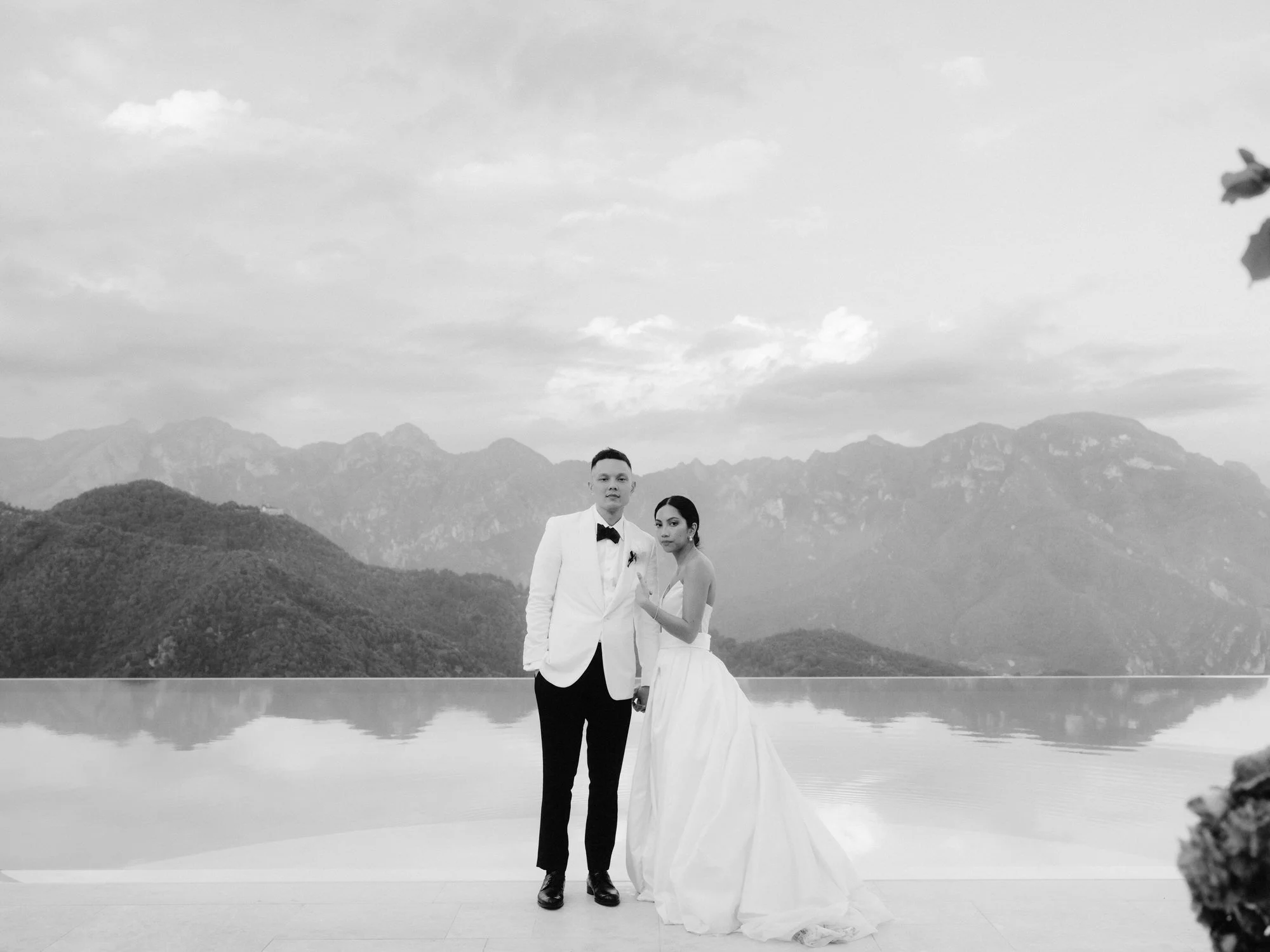 Bride and groom standing by the iconic infinity pool reflecting the mountains at Caruso, A Belmond Hotel in Ravello, Italy, photographed by Jenny Fu.
