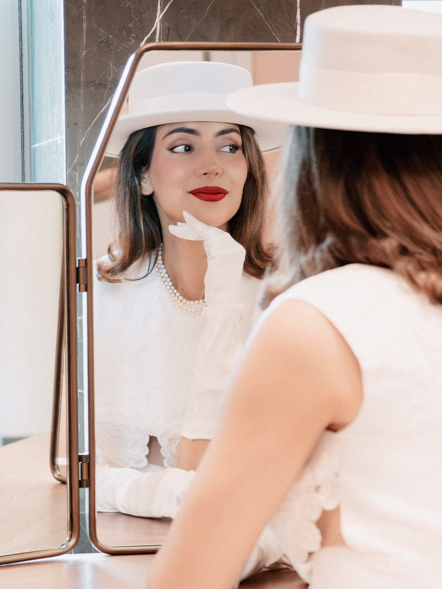 Bride in a white boater hat and red lipstick reflected in a vanity mirror while getting ready at the Waldorf Astoria New York, photographed by Jenny Fu.