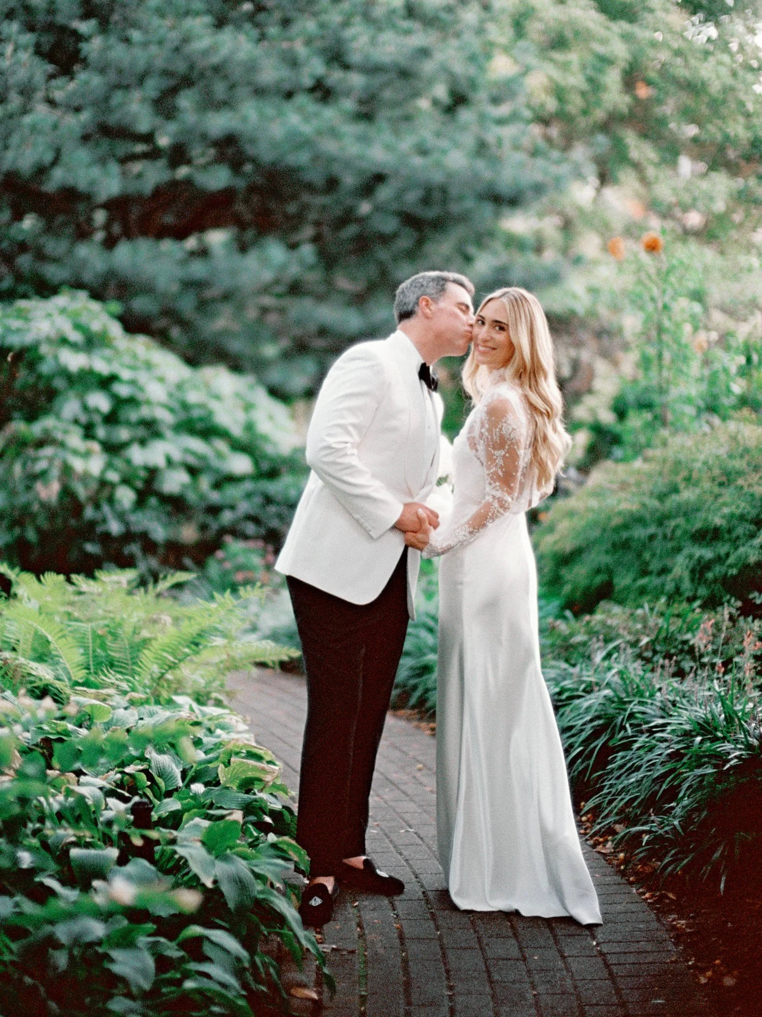 Groom kissing bride on the cheek surrounded by lush greenery at Jefferson Market Garden in the West Village, photographed by Jenny Fu.