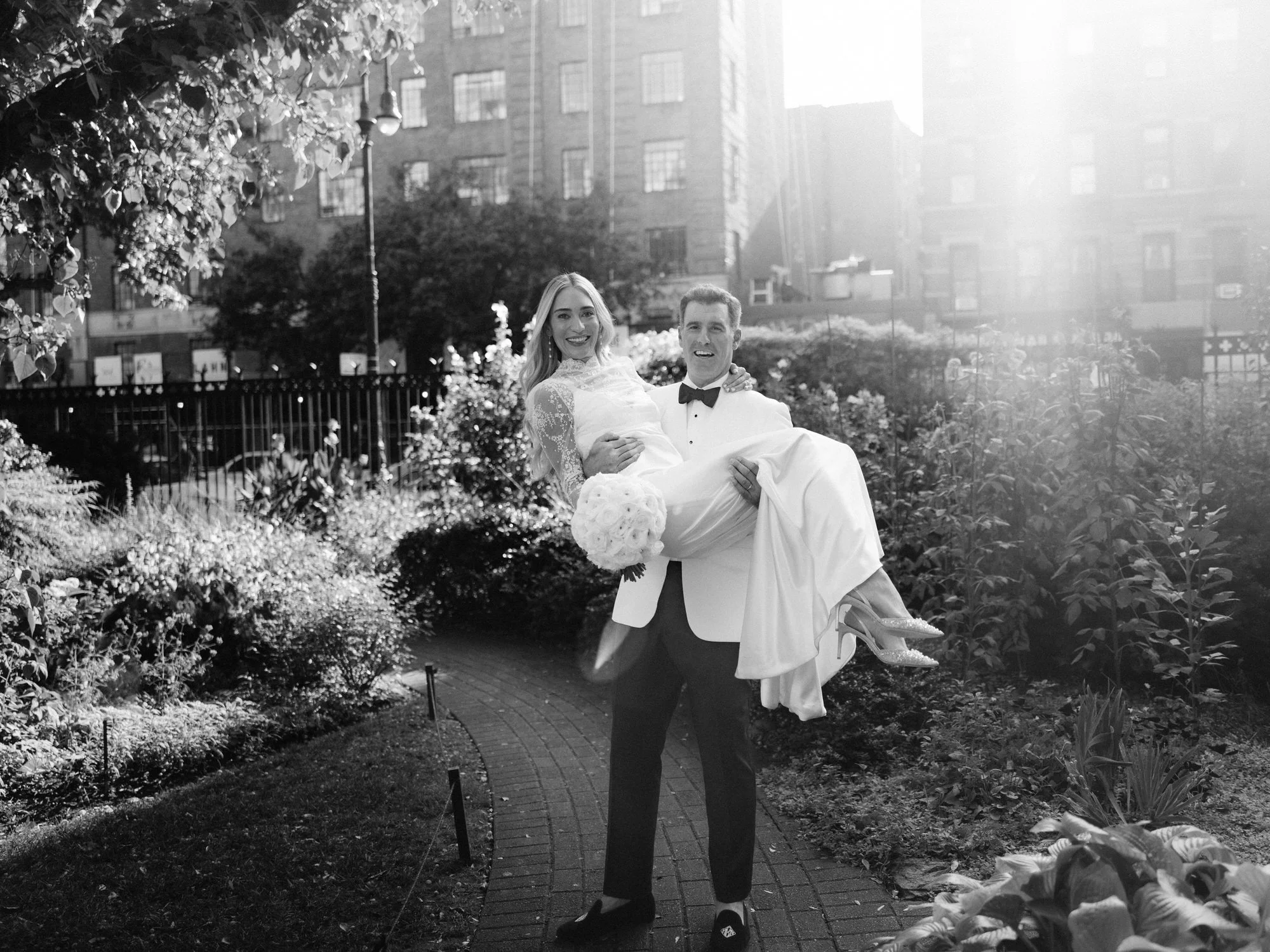 Groom carrying his bride through the sunlit garden path at Jefferson Market Garden in the West Village, photographed by Jenny Fu.