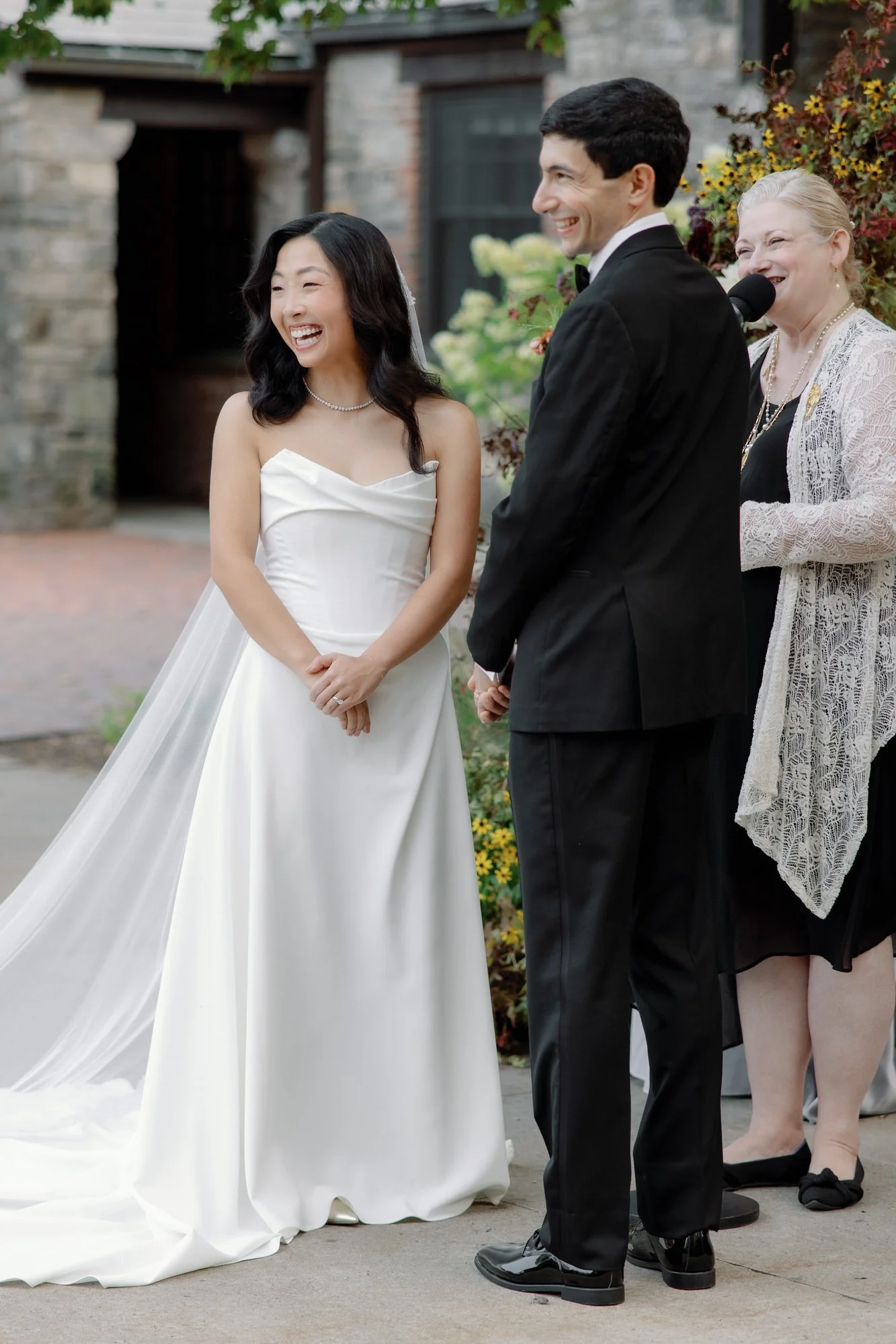 Bride laughing during the vows beside the groom and officiant in the courtyard at Blue Hill at Stone Barns, photographed by Jenny Fu.