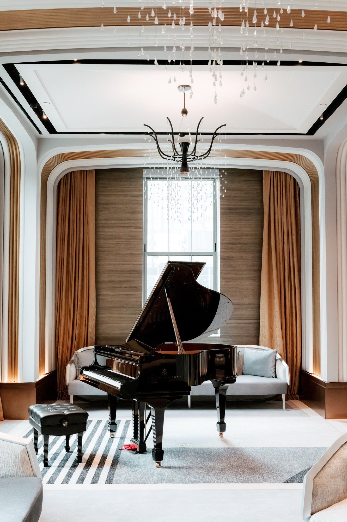 Grand piano beneath a chandelier in a sunlit suite at the Waldorf Astoria New York, photographed by Jenny Fu.