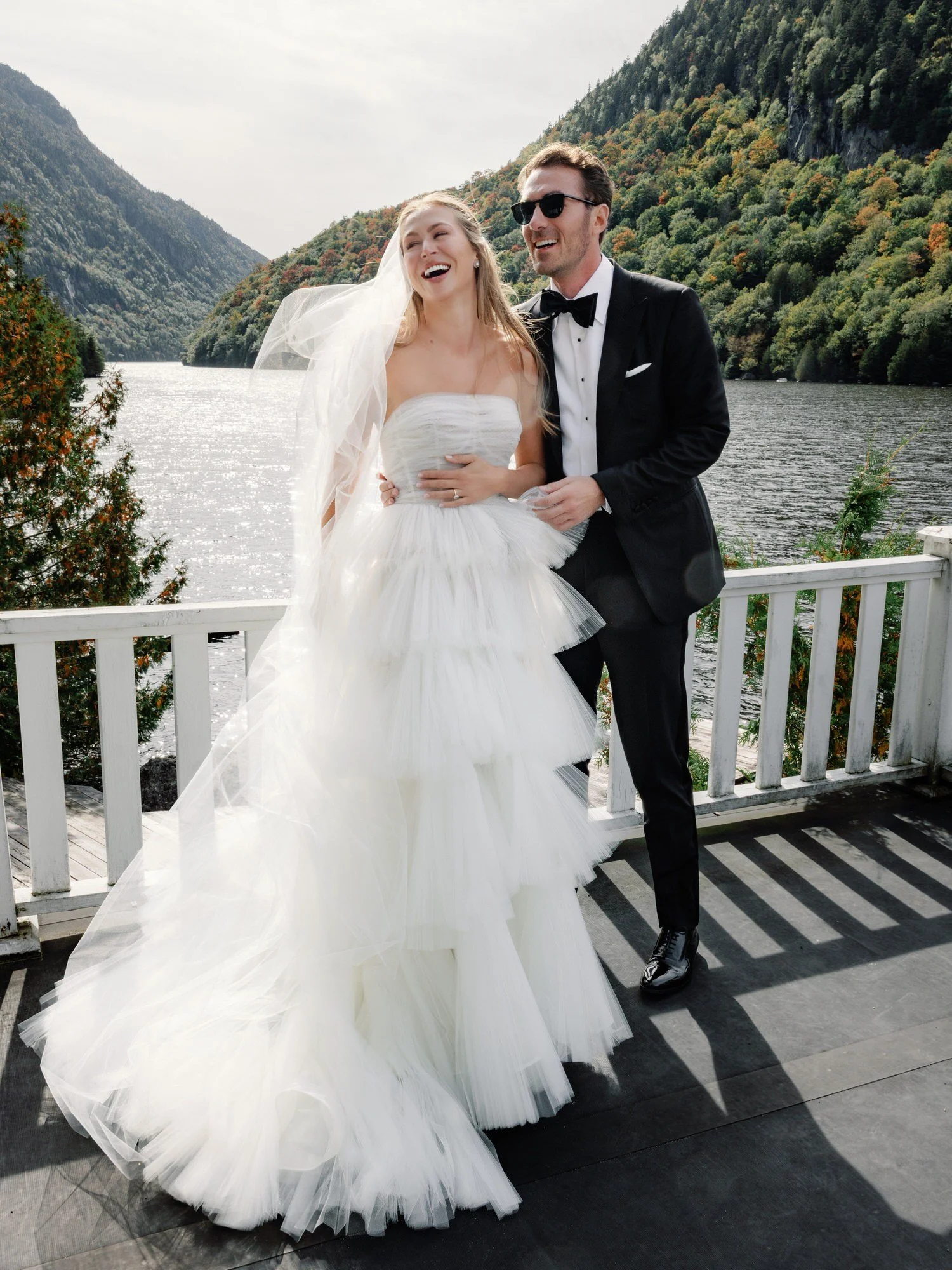 Bride and groom laughing together on lakeside deck at The Ausable Club in the Adirondacks