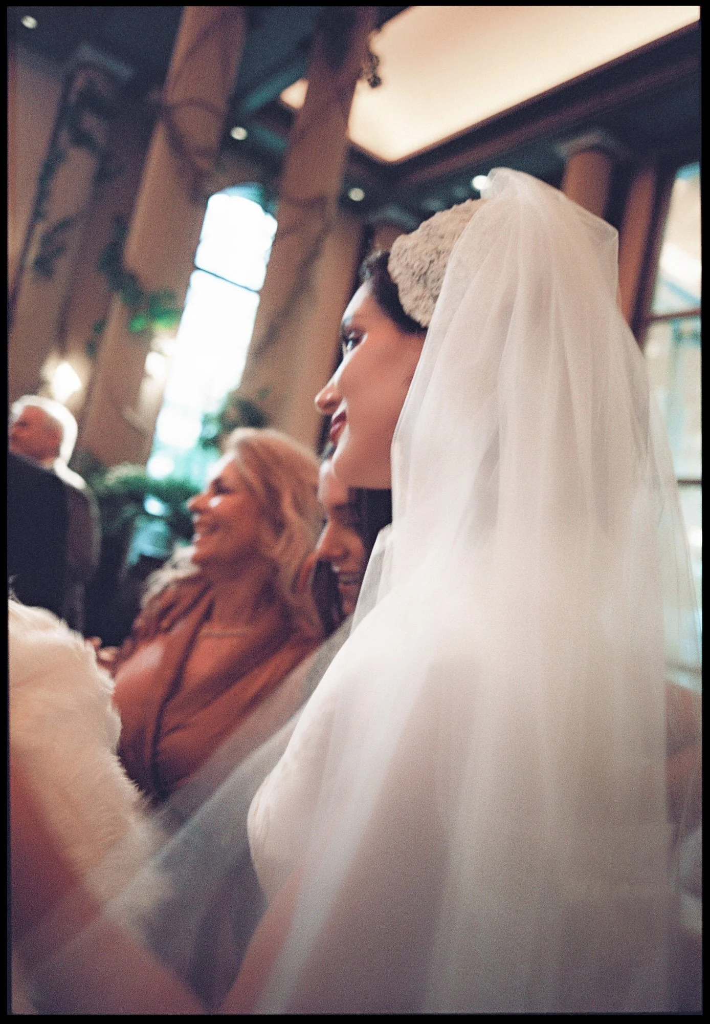 Bride in a lace cap veil seen in profile among guests at her Waldorf Astoria New York wedding reception, photographed by Jenny Fu.