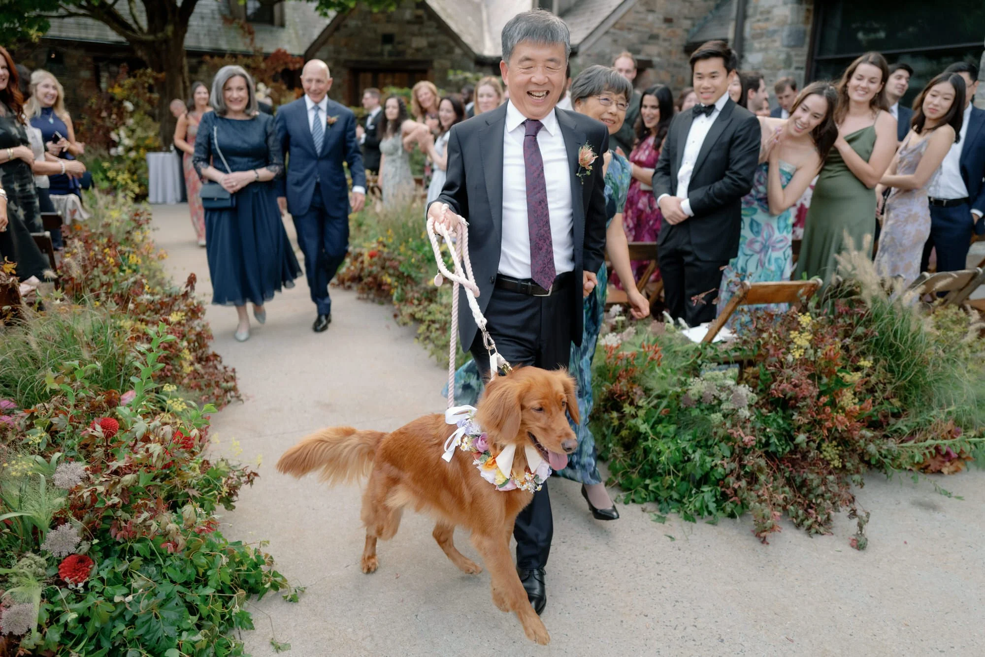 Family member walks the couple’s dog with a floral collar down the aisle as guests smile at Blue Hill at Stone Barns, photographed by Jenny Fu.