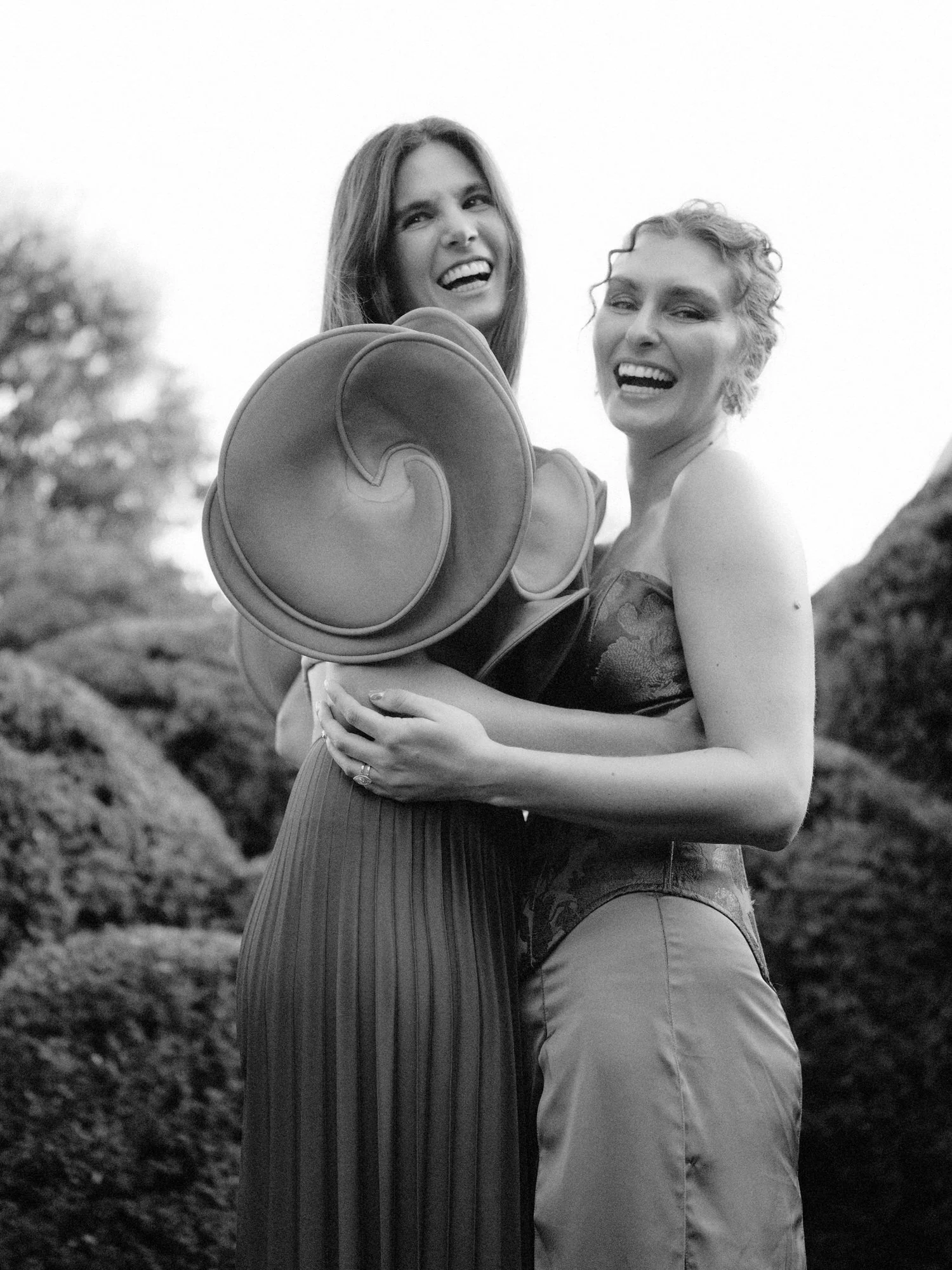 Two brides laughing in a candid black and white portrait in the garden at Valley Rock Inn in Sloatsburg, photographed by Jenny Fu.
