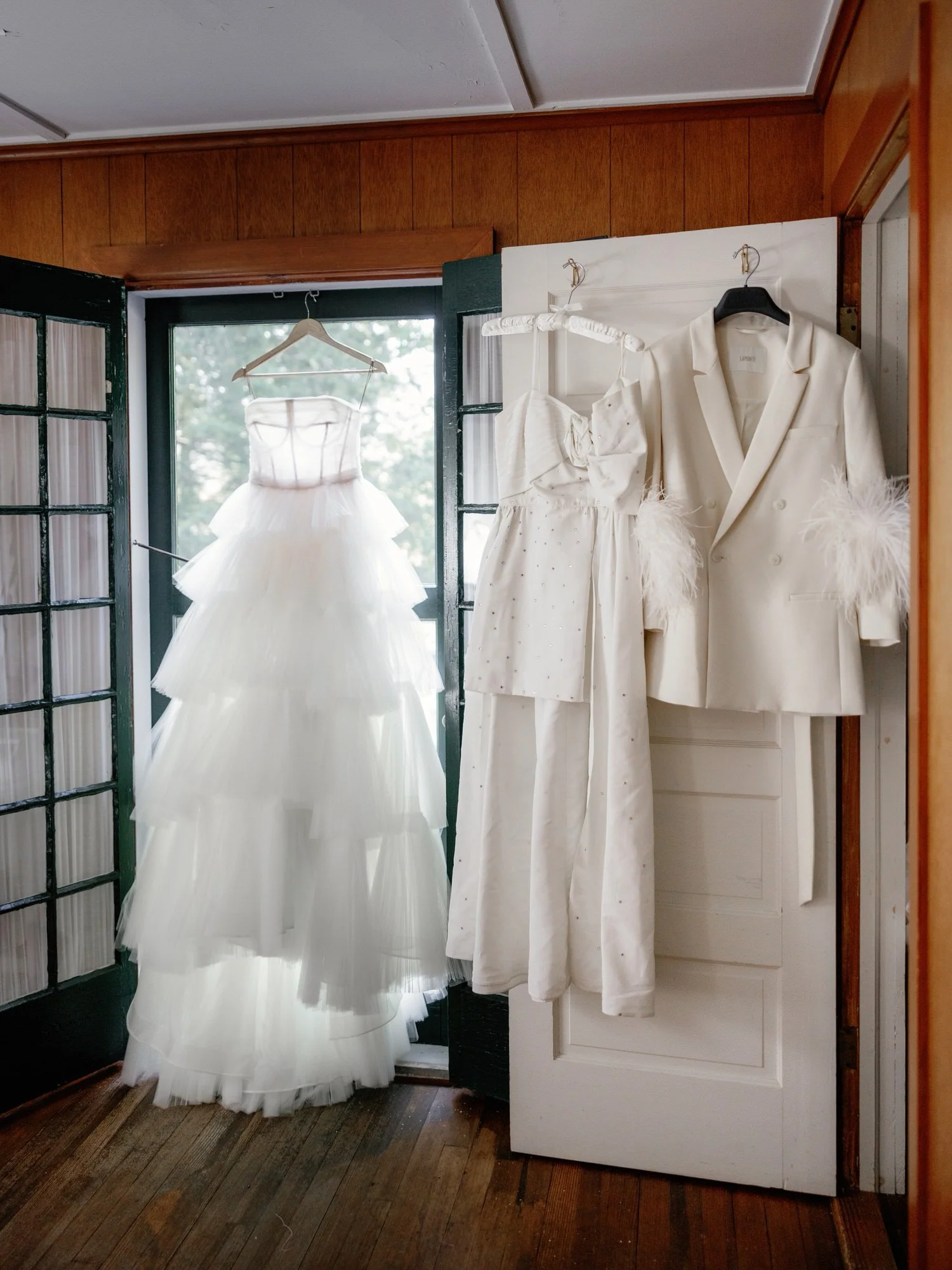 Bridal gown and white suit with feather details hanging in the getting ready suite at the Ausable Club in the Adirondacks
