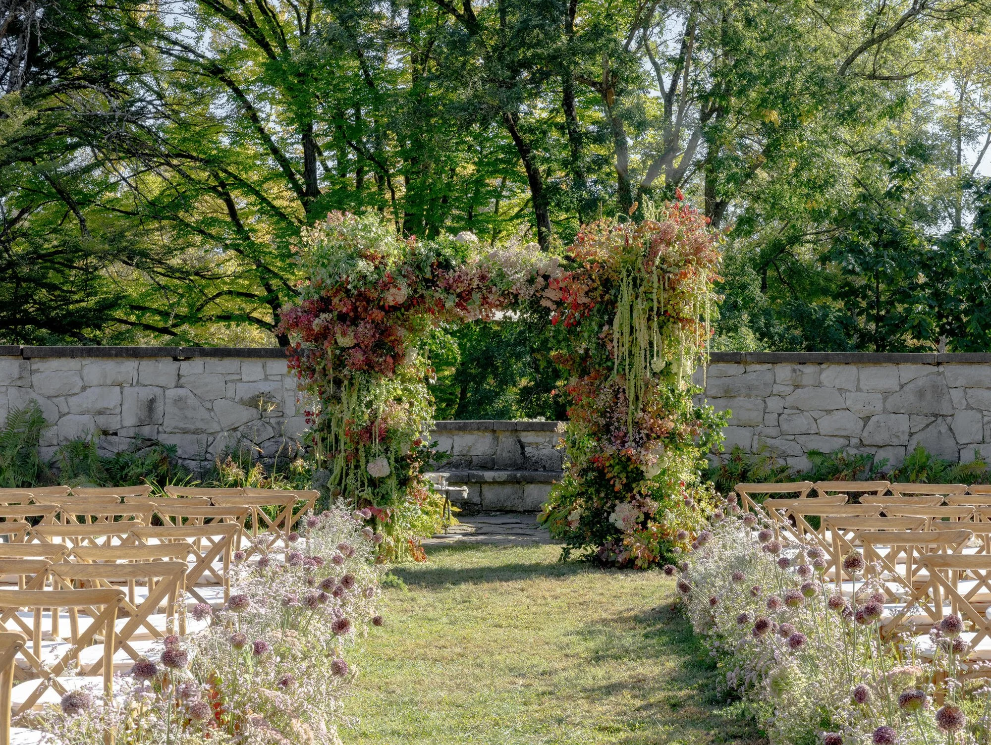 Rows of wooden crossback chairs with wild floral aisle leading to the ceremony altar in the Walled Garden at Troutbeck in Amenia, photographed by Jenny Fu.