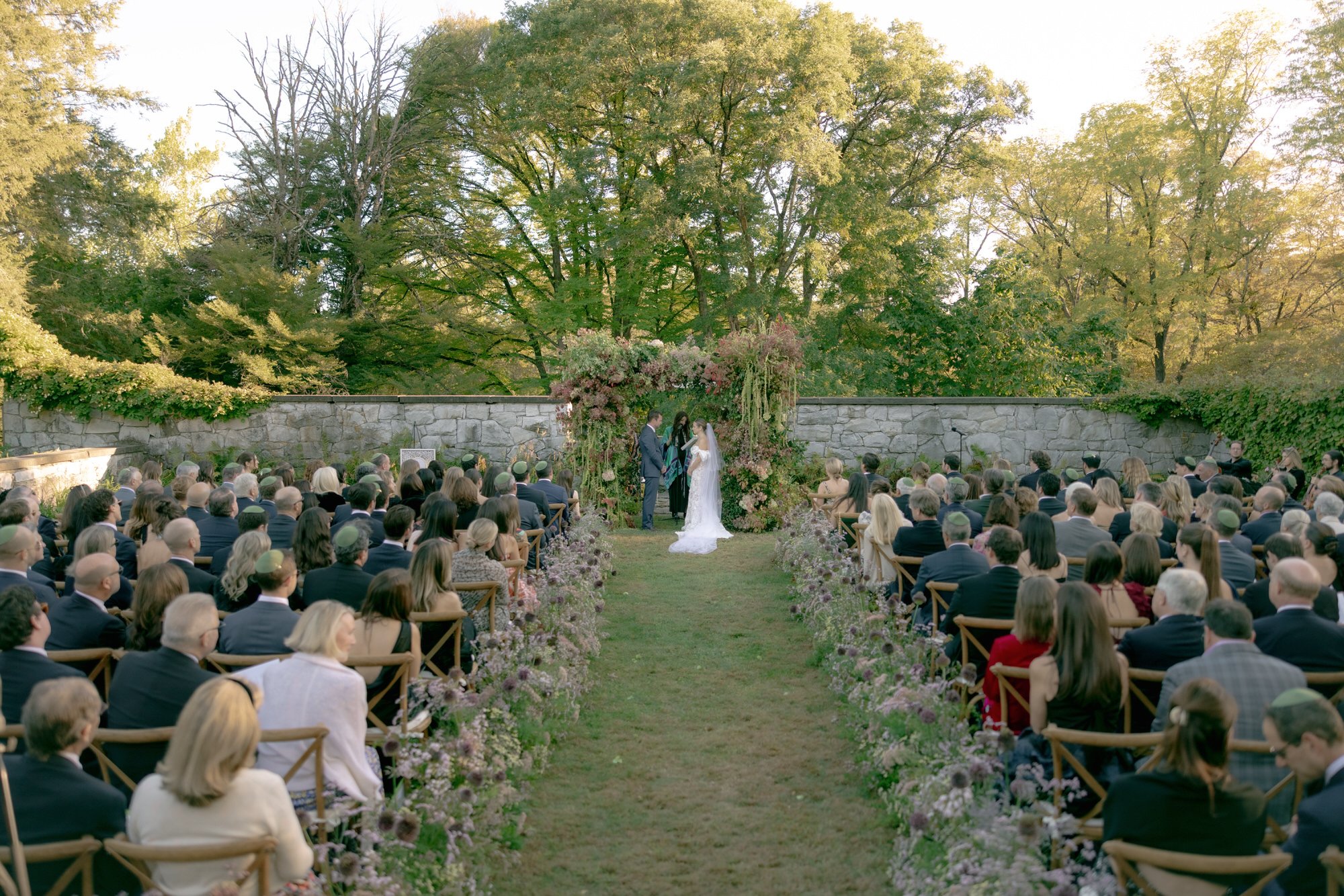 Wide view of the ceremony with guests seated and the couple under a floral altar at Troutbeck in Amenia, photographed by Jenny Fu.