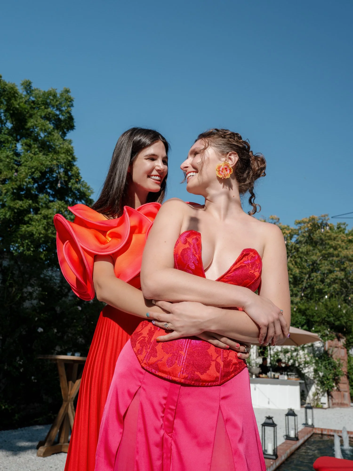 Sunlit portrait of two brides in red and pink on the terrace at Valley Rock Inn, Sloatsburg, NY, photographed by Jenny Fu.
