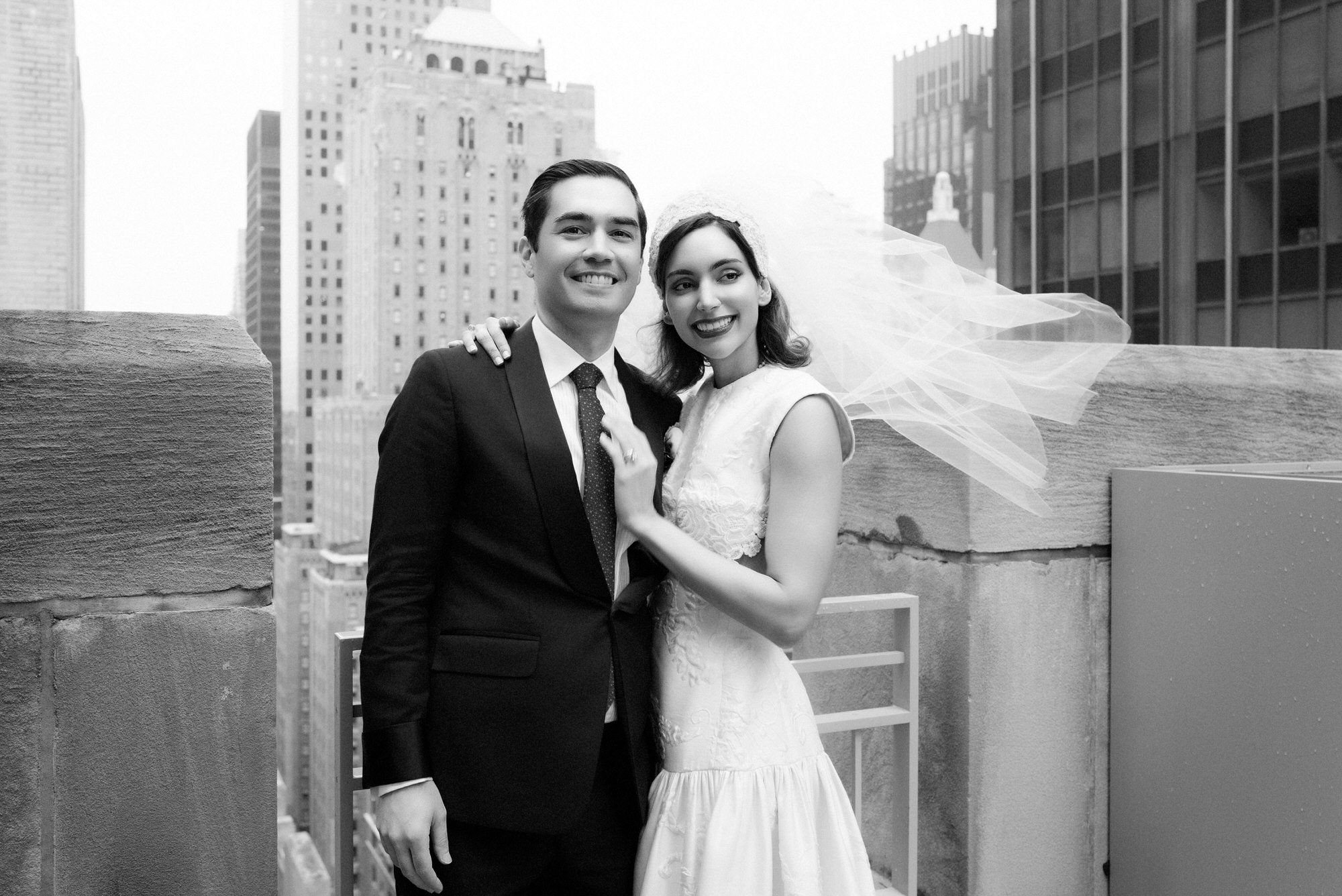 Black and white portrait of the bride and groom smiling on a terrace with the Midtown skyline at the Waldorf Astoria New York, photographed by Jenny Fu.