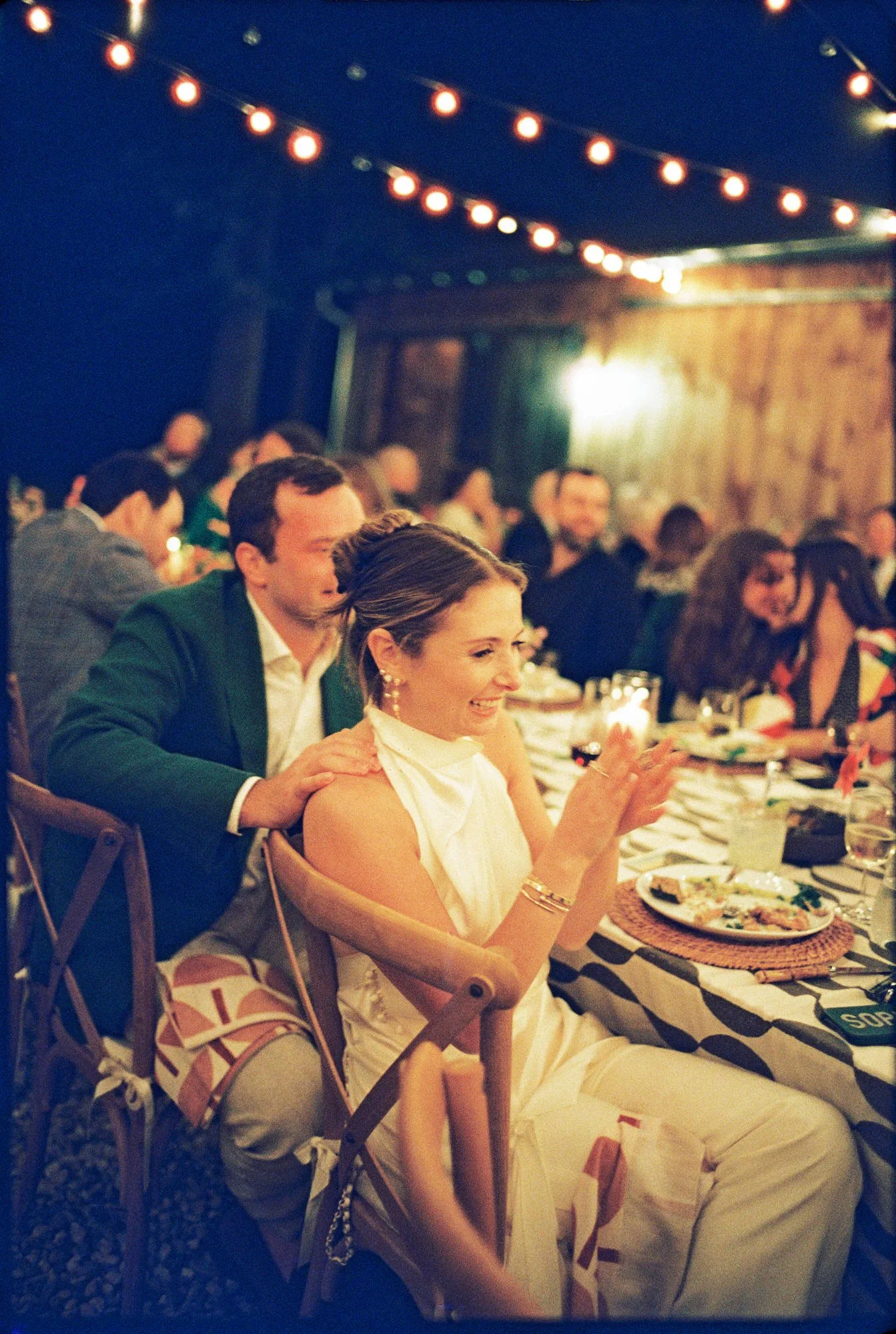 Bride clapping and laughing during toasts under string lights at Troutbeck in Amenia, photographed by Jenny Fu.