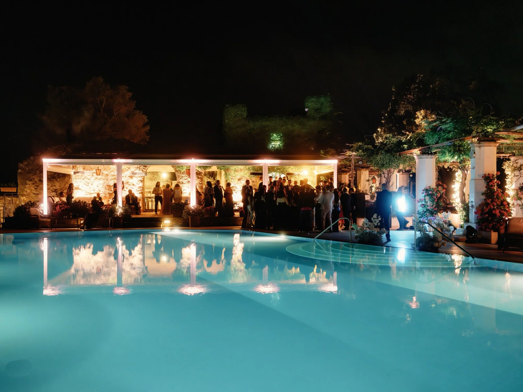 Nighttime wedding celebration reflected in the glowing blue pool at Caruso, A Belmond Hotel in Ravello, Italy, photographed by Jenny Fu.