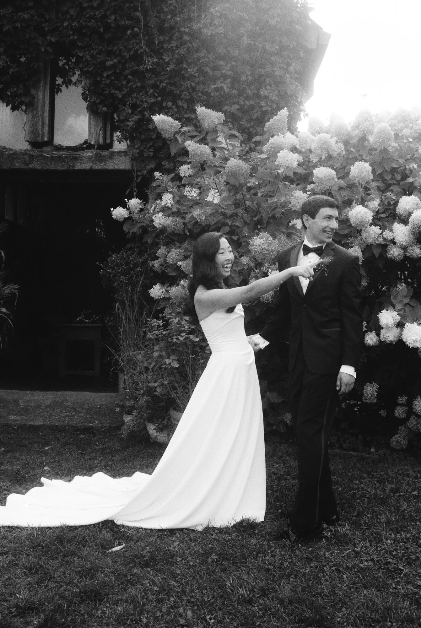 Playful first look by the hydrangeas in black and white as the bride taps the groom's shoulder at Blue Hill at Stone Barns, photographed by Jenny Fu.