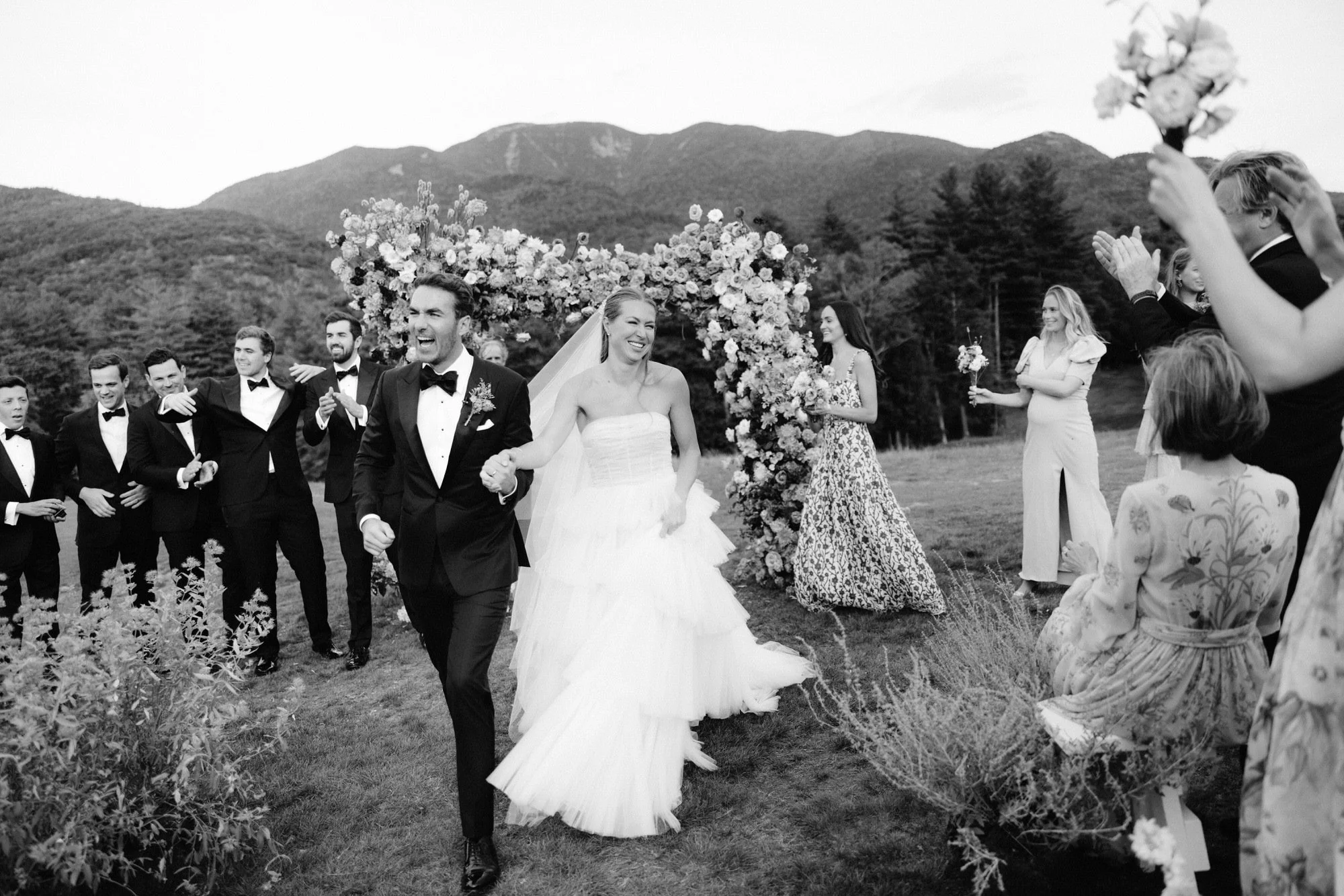 Bride and groom walking down the aisle smiling as guests cheer at The Ausable Club in the Adirondacks