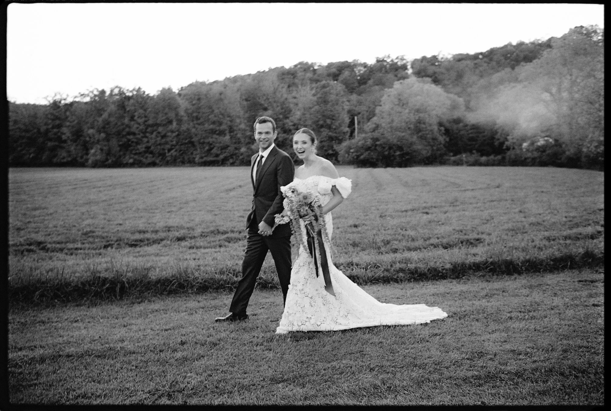 Bride and groom smiling as they walk the field at dusk at Troutbeck in Amenia, New York, photographed by Jenny Fu.