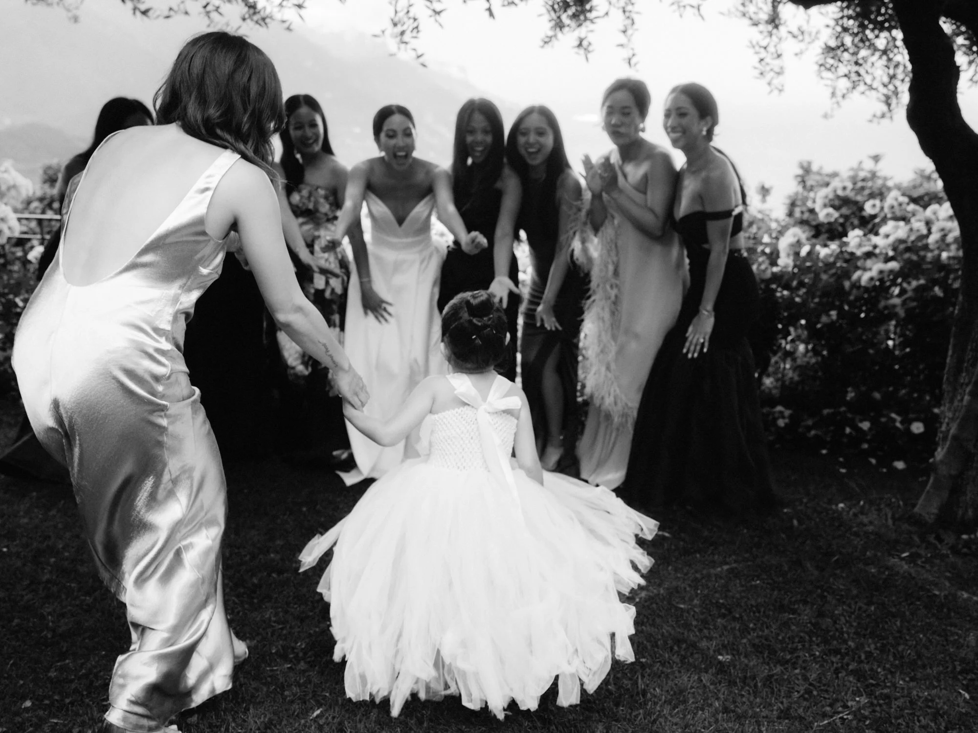 Bride and bridesmaids laughing as the flower girl runs toward them under the olive trees at Caruso, A Belmond Hotel in Ravello, Italy, photographed by Jenny Fu.
