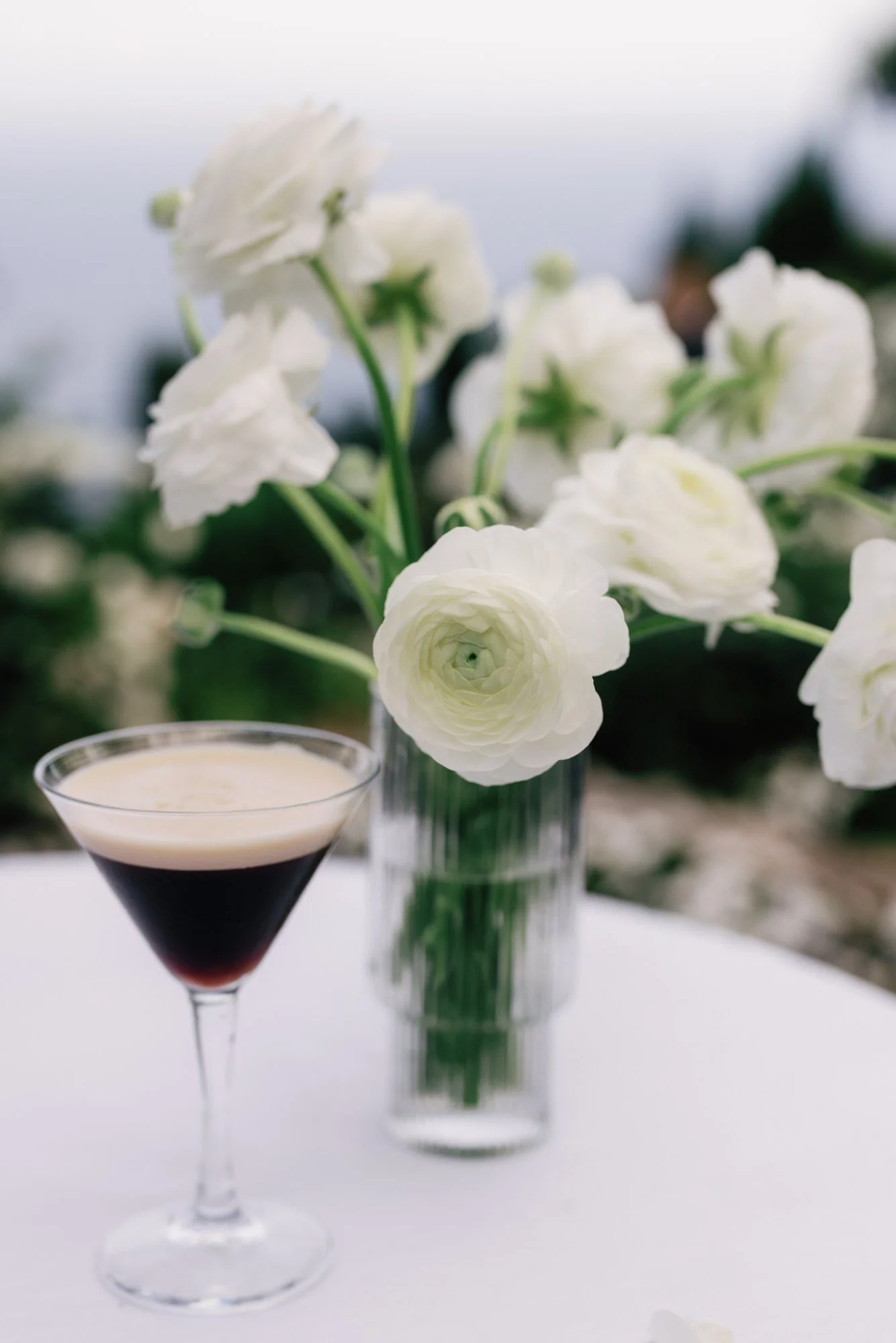 Cocktail table styled with an espresso martini and white ranunculus arrangement overlooking the sea at Caruso, A Belmond Hotel in Ravello, Italy, photographed by Jenny Fu.