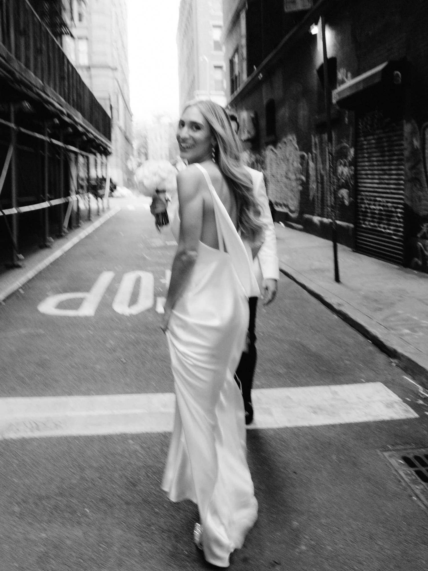 Bride glancing back playfully while walking down a cobblestone street in Soho with her groom following behind, photographed by Jenny Fu.