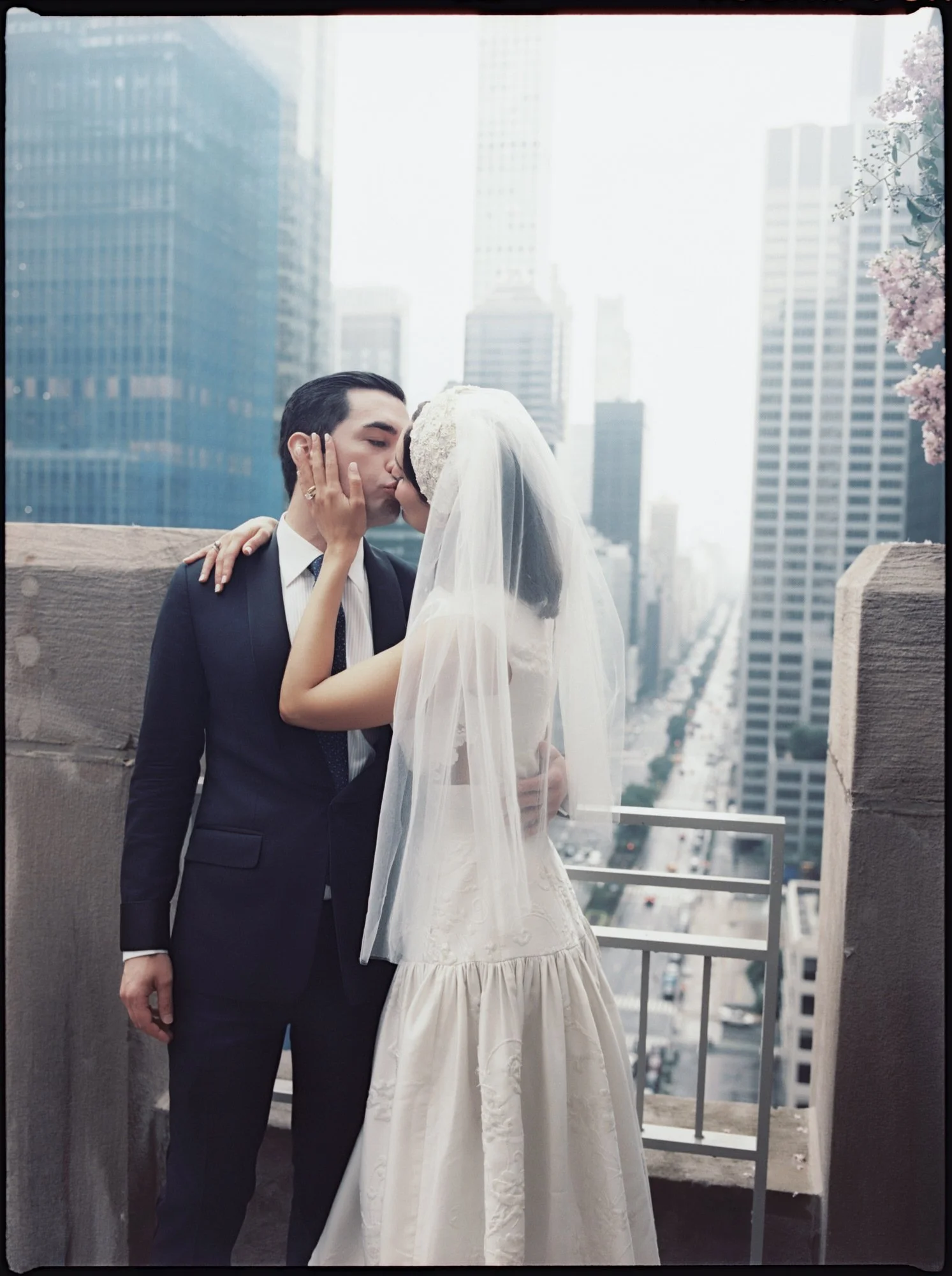 Bride and groom kissing on a terrace with Midtown skyscrapers in the mist above Park Avenue at the Waldorf Astoria New York, photographed by Jenny Fu.