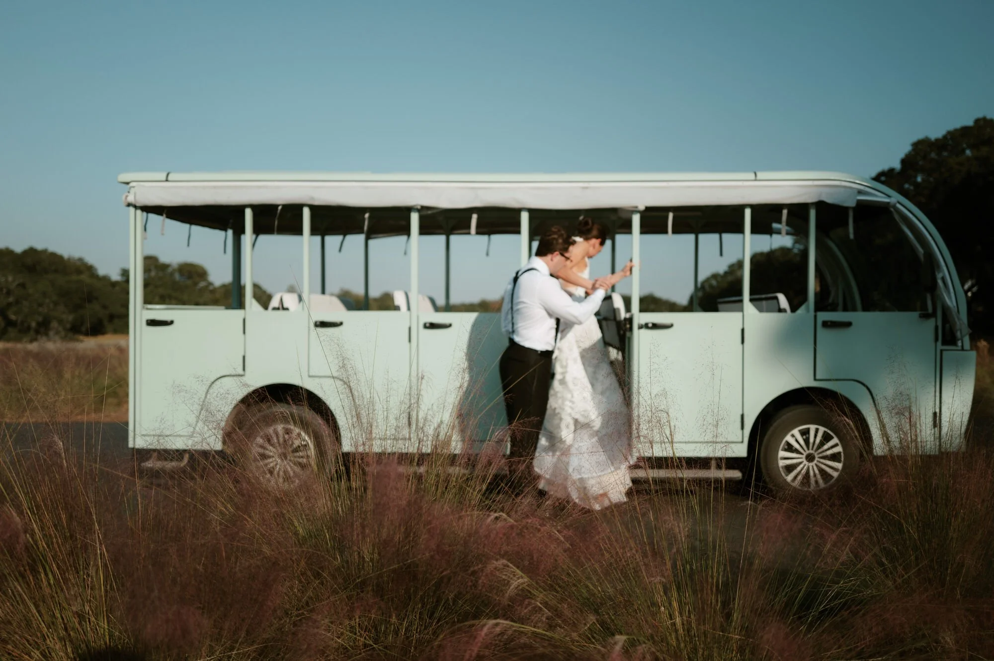 Bride and groom walking beside a mint-green trolley surrounded by golden light and wild grasses at The Dunlin, Auberge, photographed by Jenny Fu.