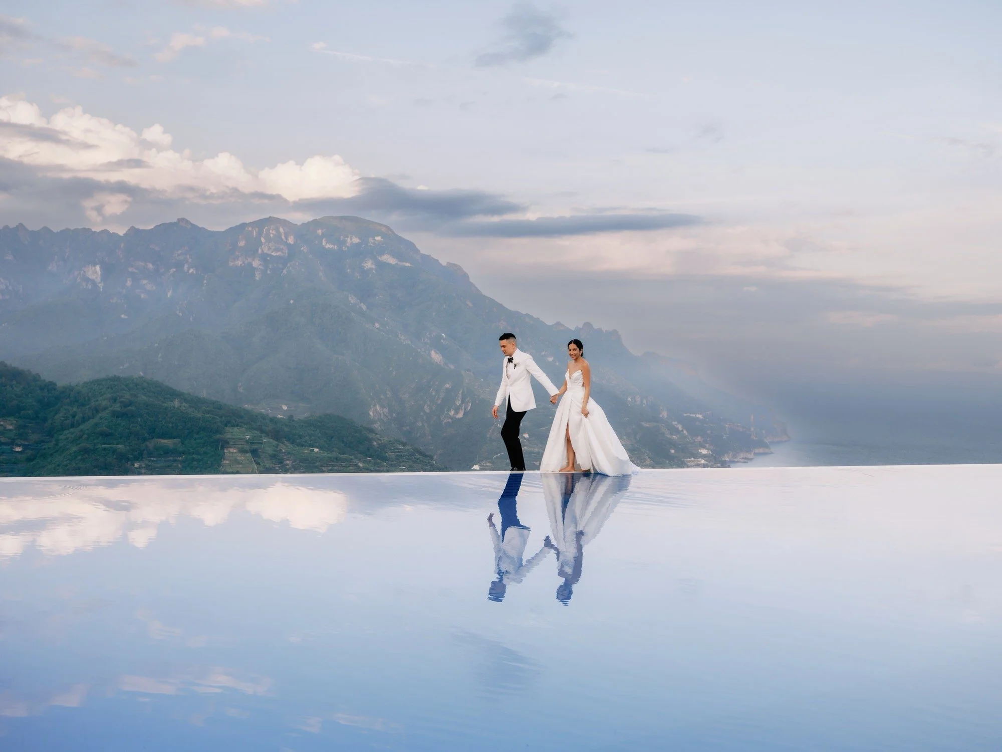 Bride and groom walking along the edge of the infinity pool with sweeping coastal views at Caruso, A Belmond Hotel in Ravello, Italy, photographed by Jenny Fu.