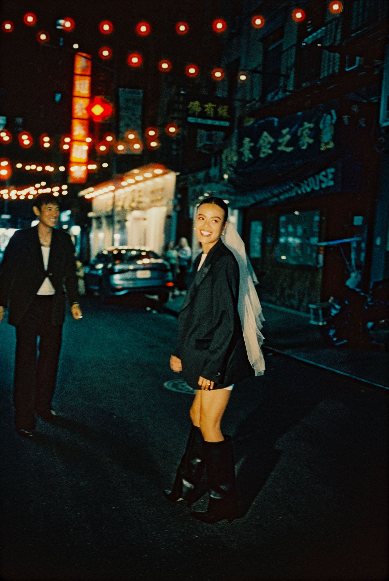Bride smiling beneath red lantern string lights in a Wong Kar-Wai inspired Chinatown street scene, photographed by Jenny Fu shot on film.