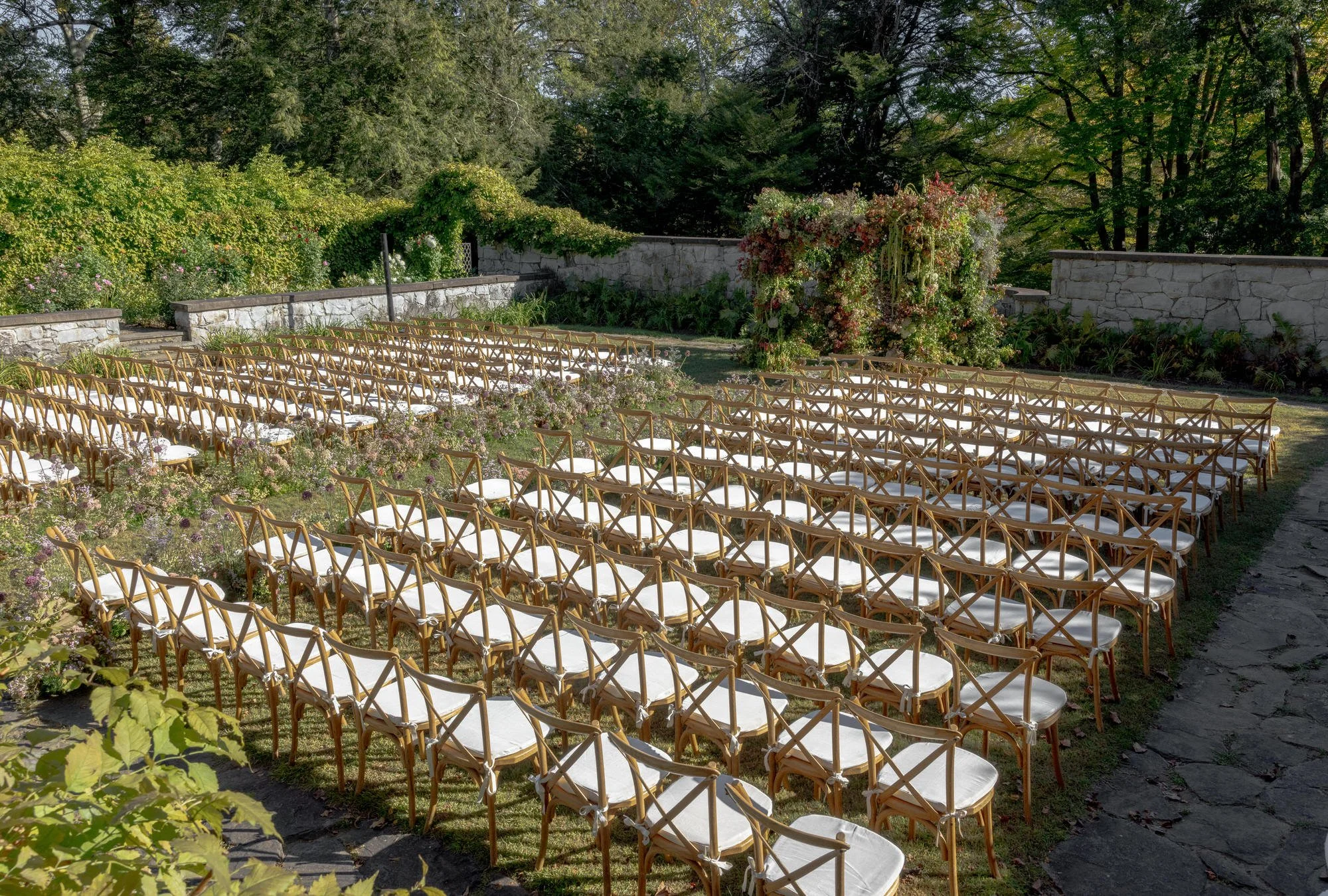 Rows of cross-back chairs leading to a lush floral arch in the walled garden at Troutbeck in Amenia, New York, photographed by Jenny Fu.