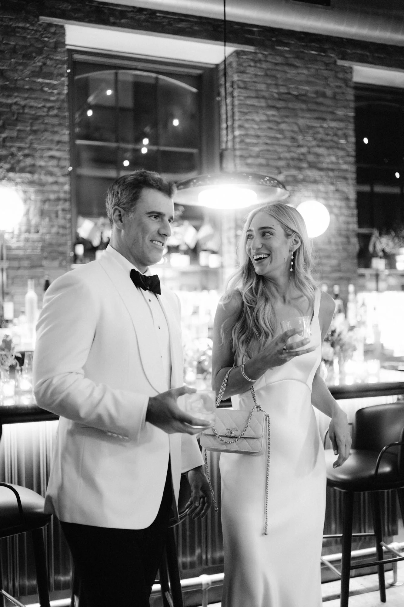 Bride and groom laughing together over cocktails beneath soft pendant lighting at Torrisi in Manhattan, photographed by Jenny Fu.