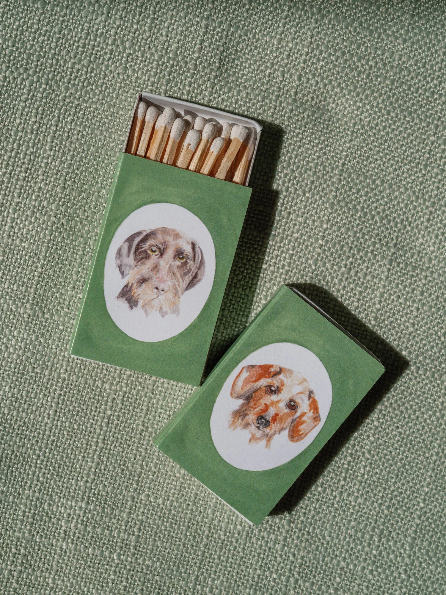 Personalized matchboxes featuring watercolor dog portraits styled on textured fabric at Troutbeck in Amenia, photographed by Jenny Fu.