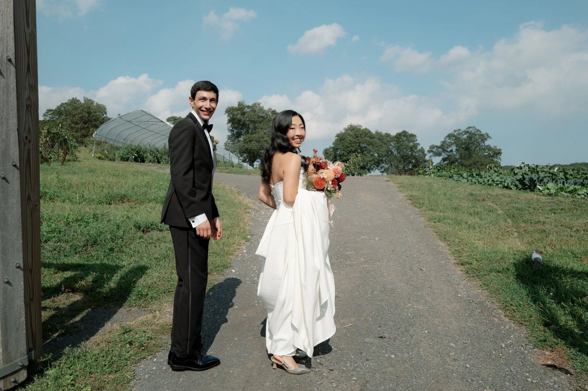Bride and groom walking up the farm path and smiling back toward the camera at Blue Hill at Stone Barns, photographed by Jenny Fu.