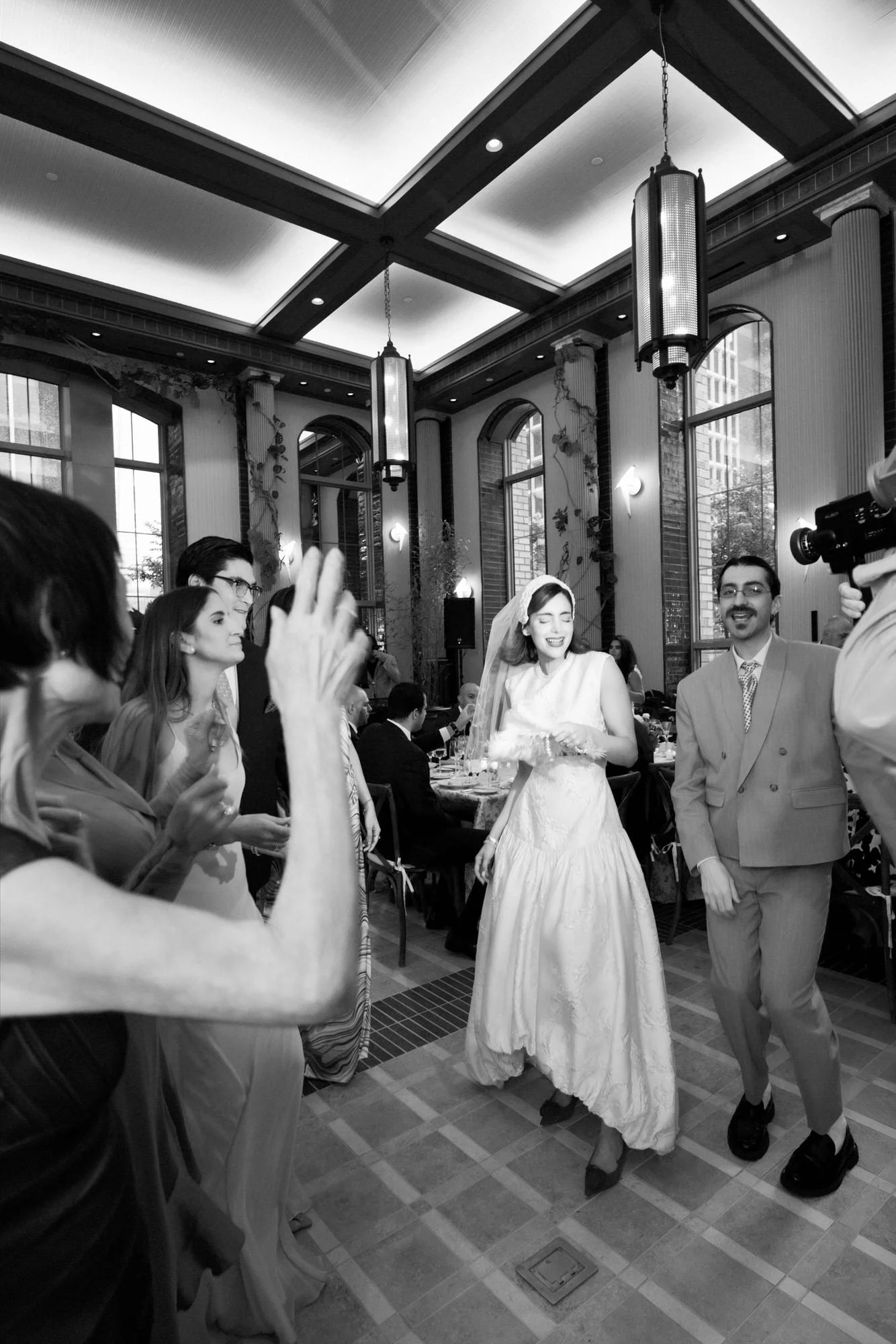 Black and white photo of the newlyweds entering their reception to cheering guests at the Waldorf Astoria New York, photographed by Jenny Fu.