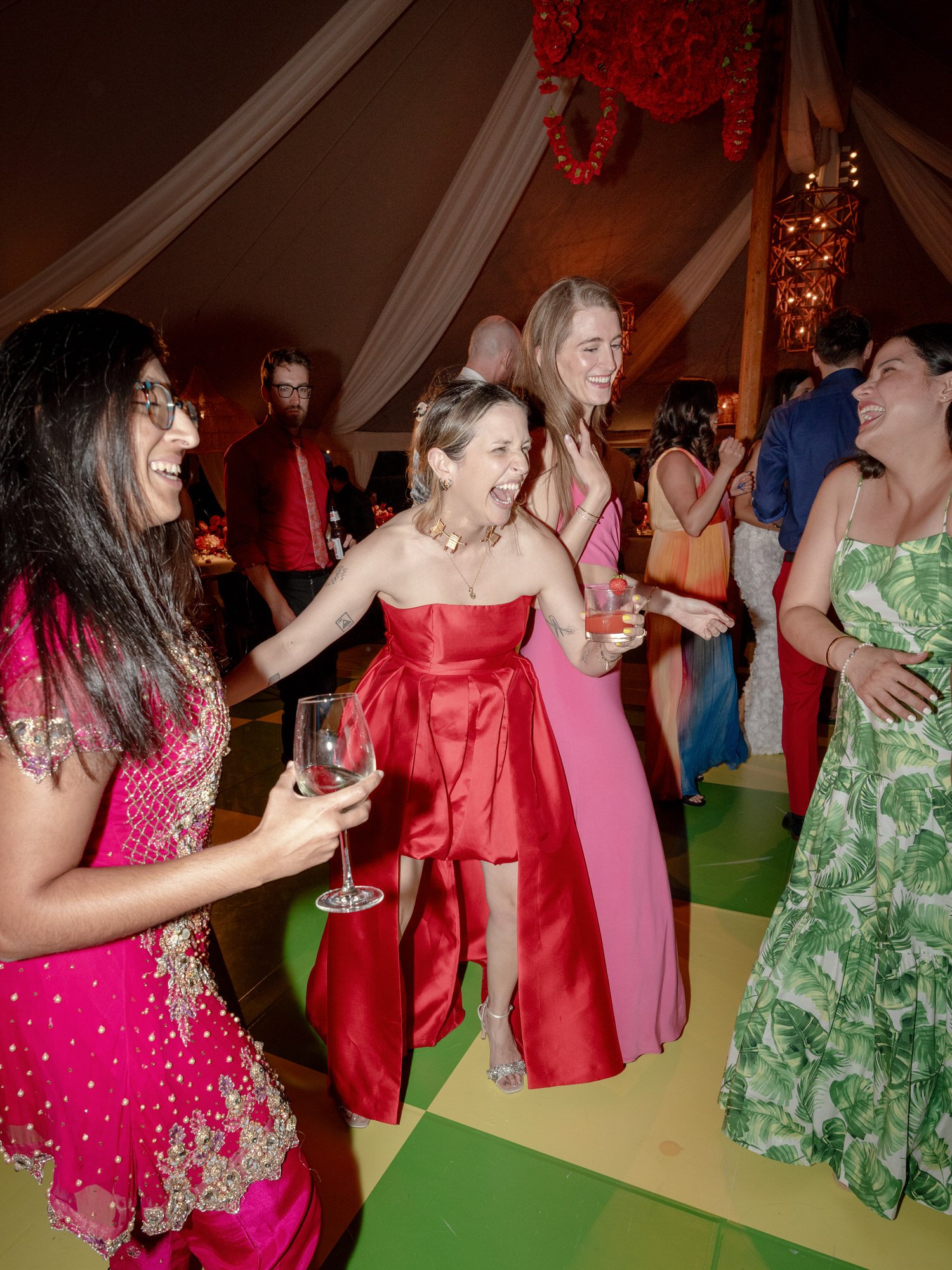 Guests laughing and dancing in vibrant dresses beneath the draped tent ceiling at Valley Rock Inn in Sloatsburg, photographed by Jenny Fu.