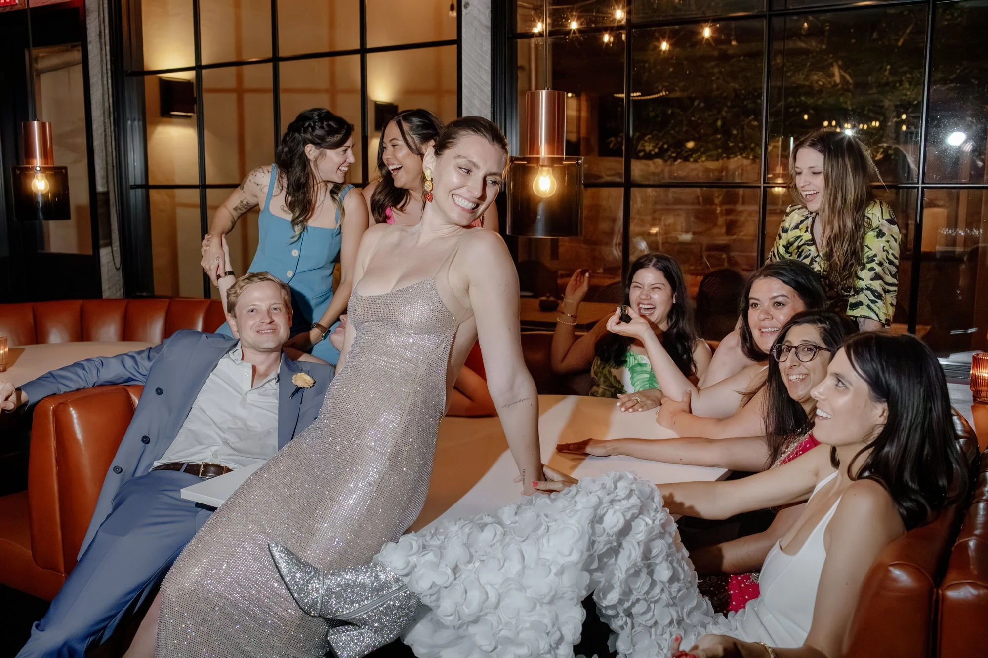Bride in a sparkling gown surrounded by friends laughing together in the cozy after-party lounge at Valley Rock Inn in Sloatsburg, photographed by Jenny Fu.