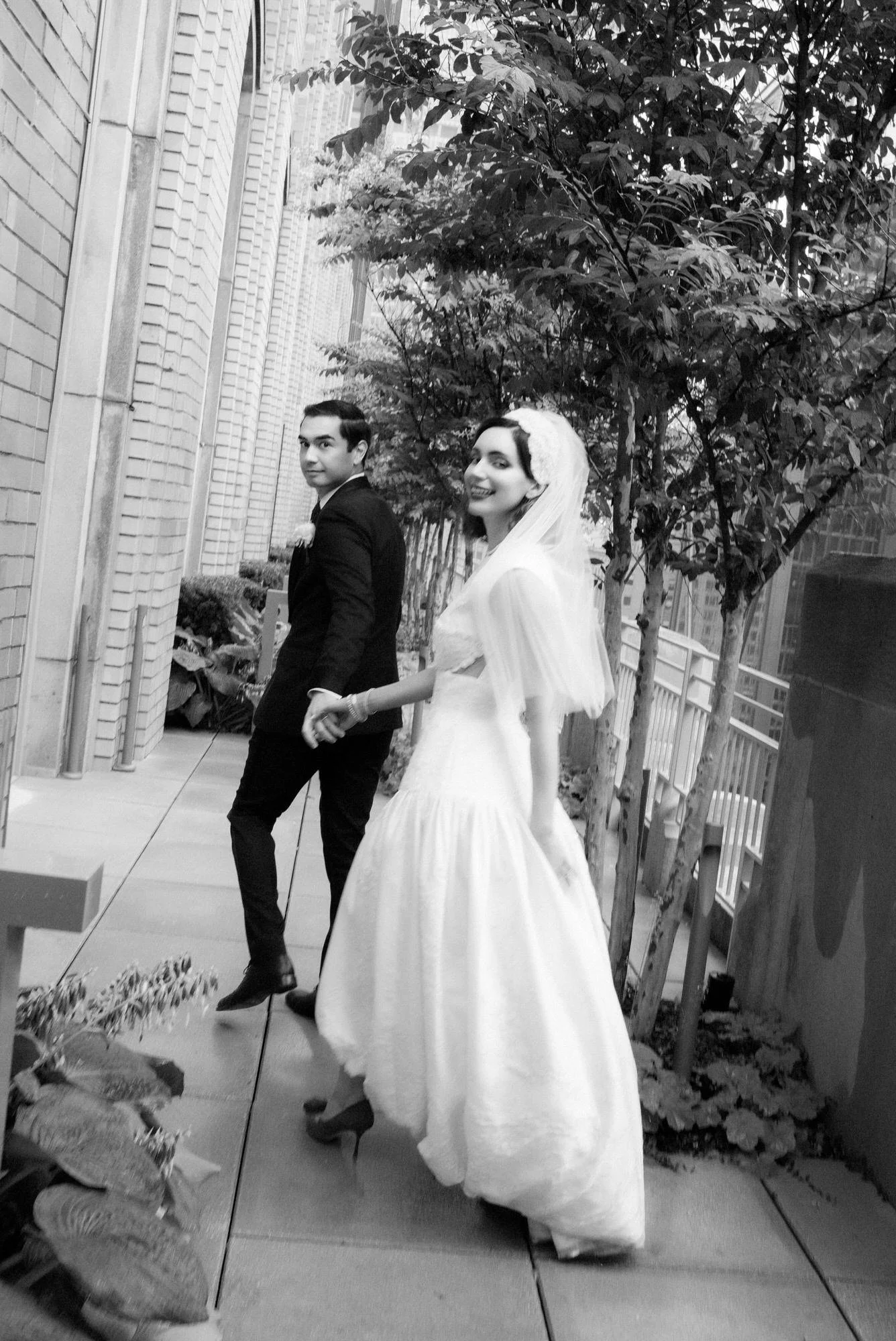 Black and white photo of the bride and groom walking hand in hand on a planted terrace at the Waldorf Astoria New York, photographed by Jenny Fu.