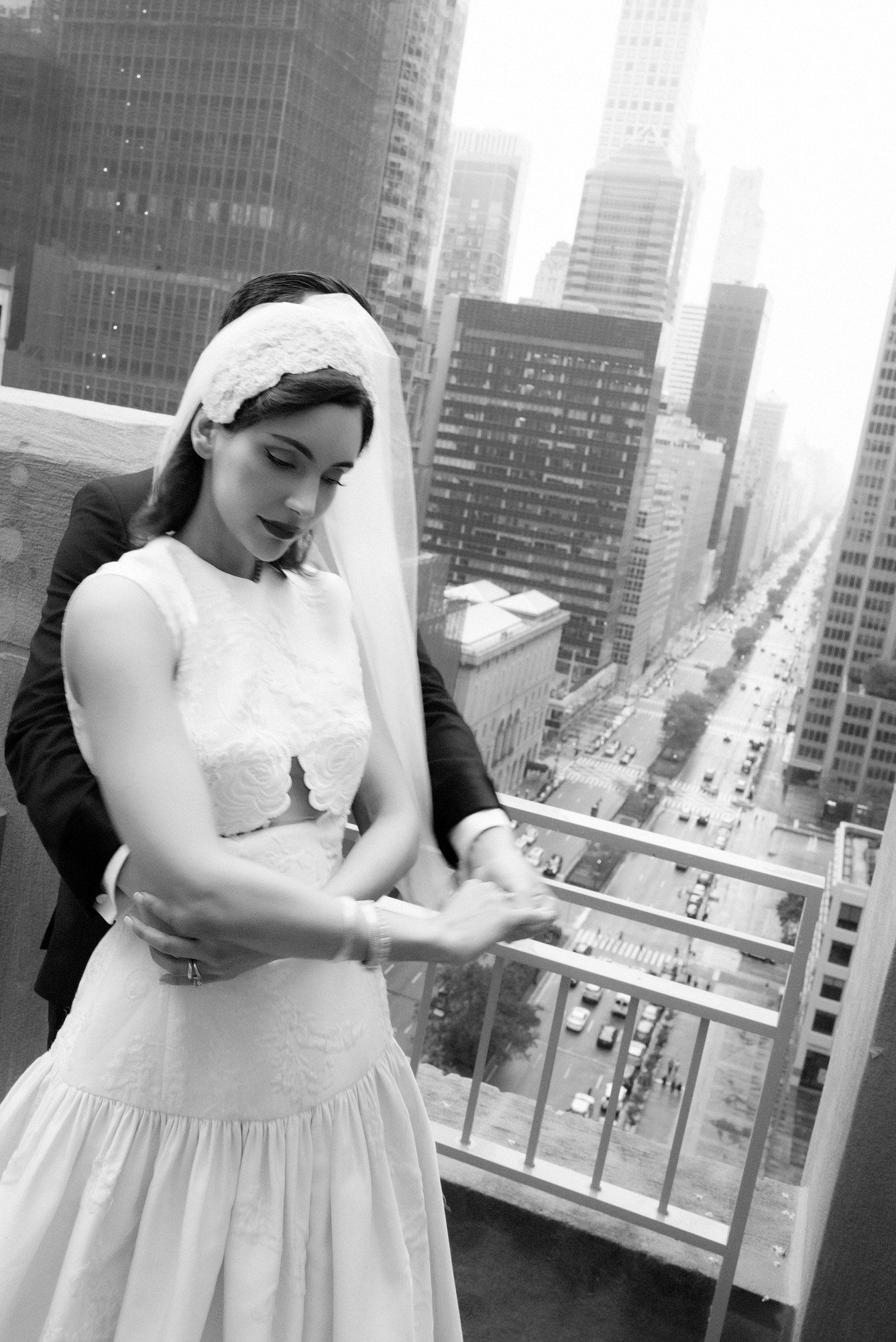 Black and white portrait of the groom embracing his bride on a terrace high above Park Avenue at the Waldorf Astoria New York, photographed by Jenny Fu.