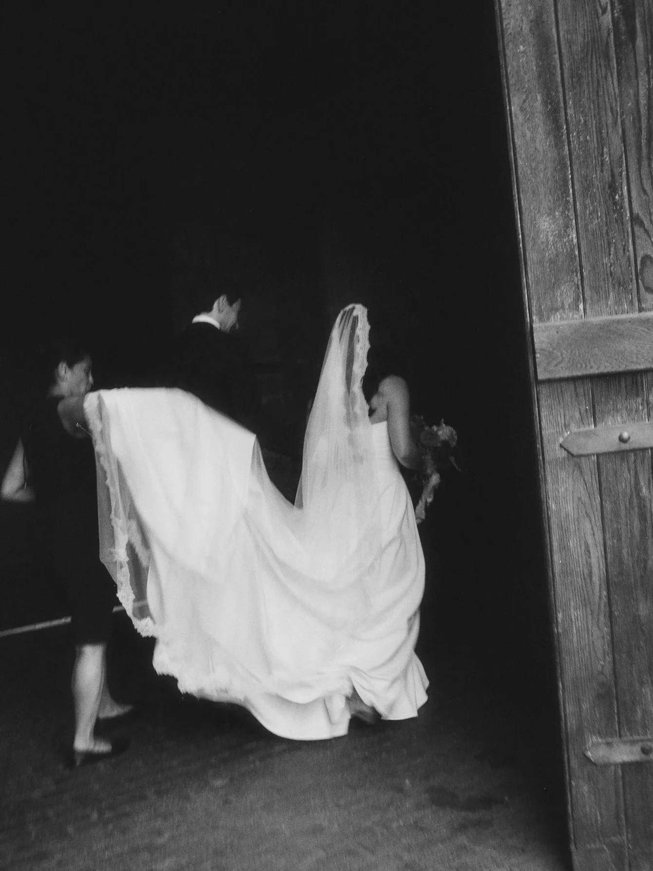 Black and white photo of a bride and groom entering the barn, her train gathered, at Blue Hill at Stone Barns