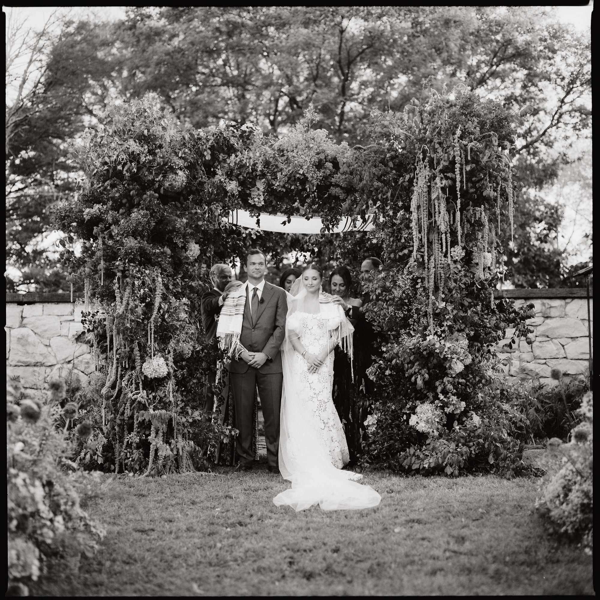 Bride and groom exchanging vows under a lush floral chuppah at Troutbeck in Amenia, photographed by Jenny Fu.