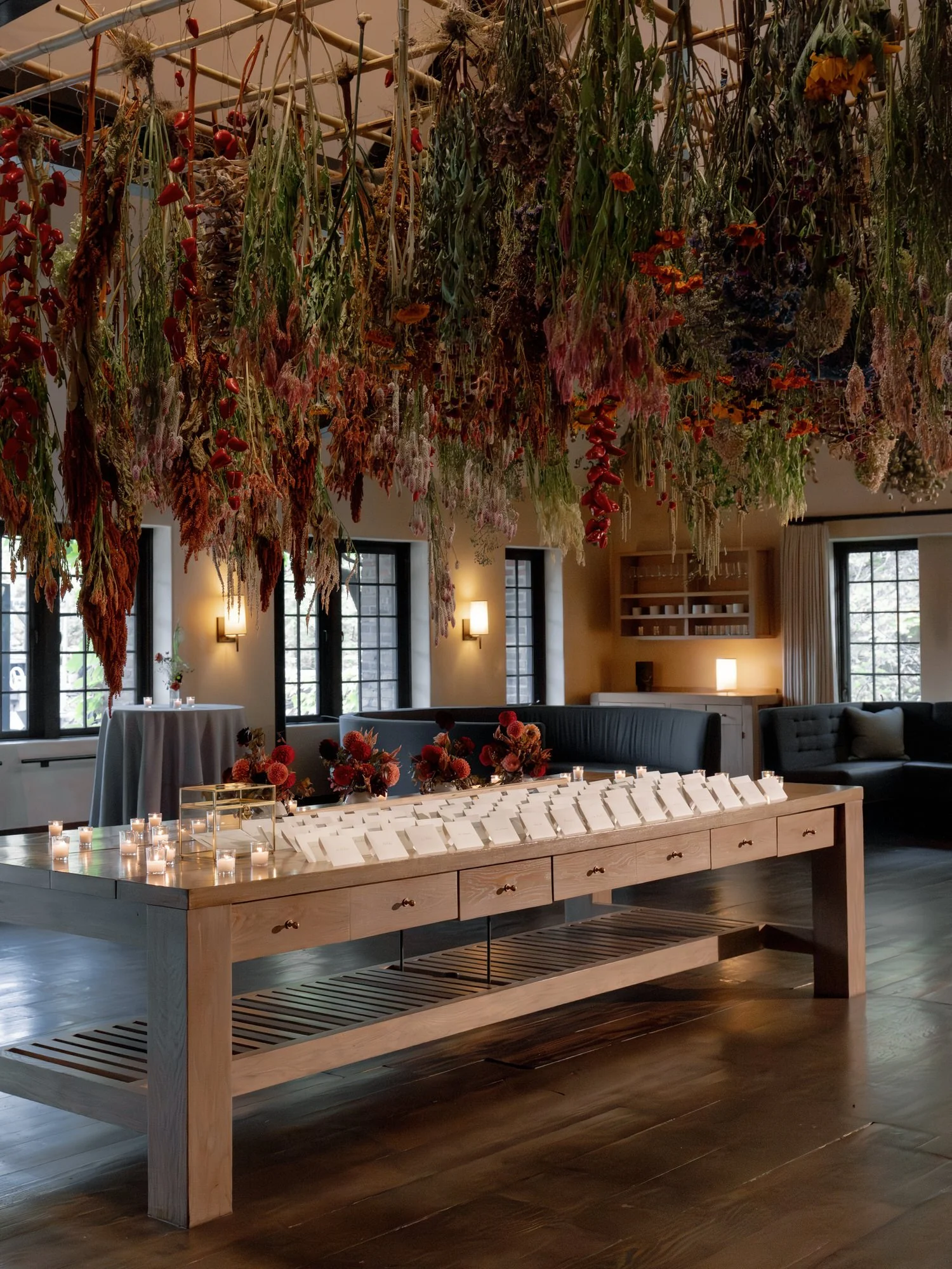 Escort card display beneath hanging dried botanicals with candlelight in the lounge at Blue Hill at Stone Barns, photographed by Jenny Fu.