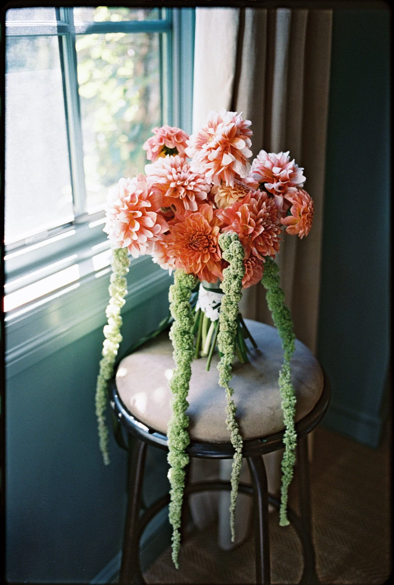 Coral dahlia and green amaranthus arrangement styled on a stool beside a window at Troutbeck in Amenia, photographed by Jenny Fu.