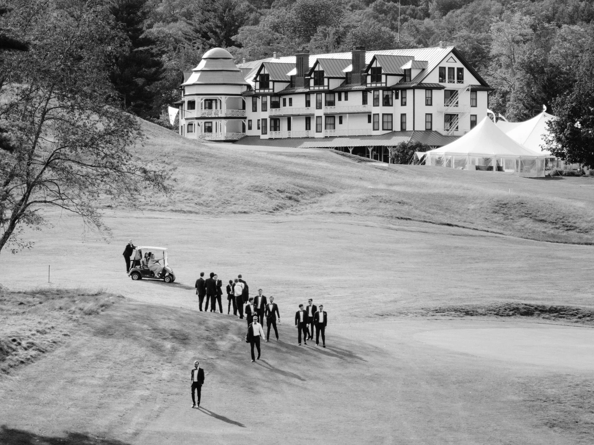 Group of groomsmen in tuxedos walking across the golf course at the Ausable Club in the Adirondacks