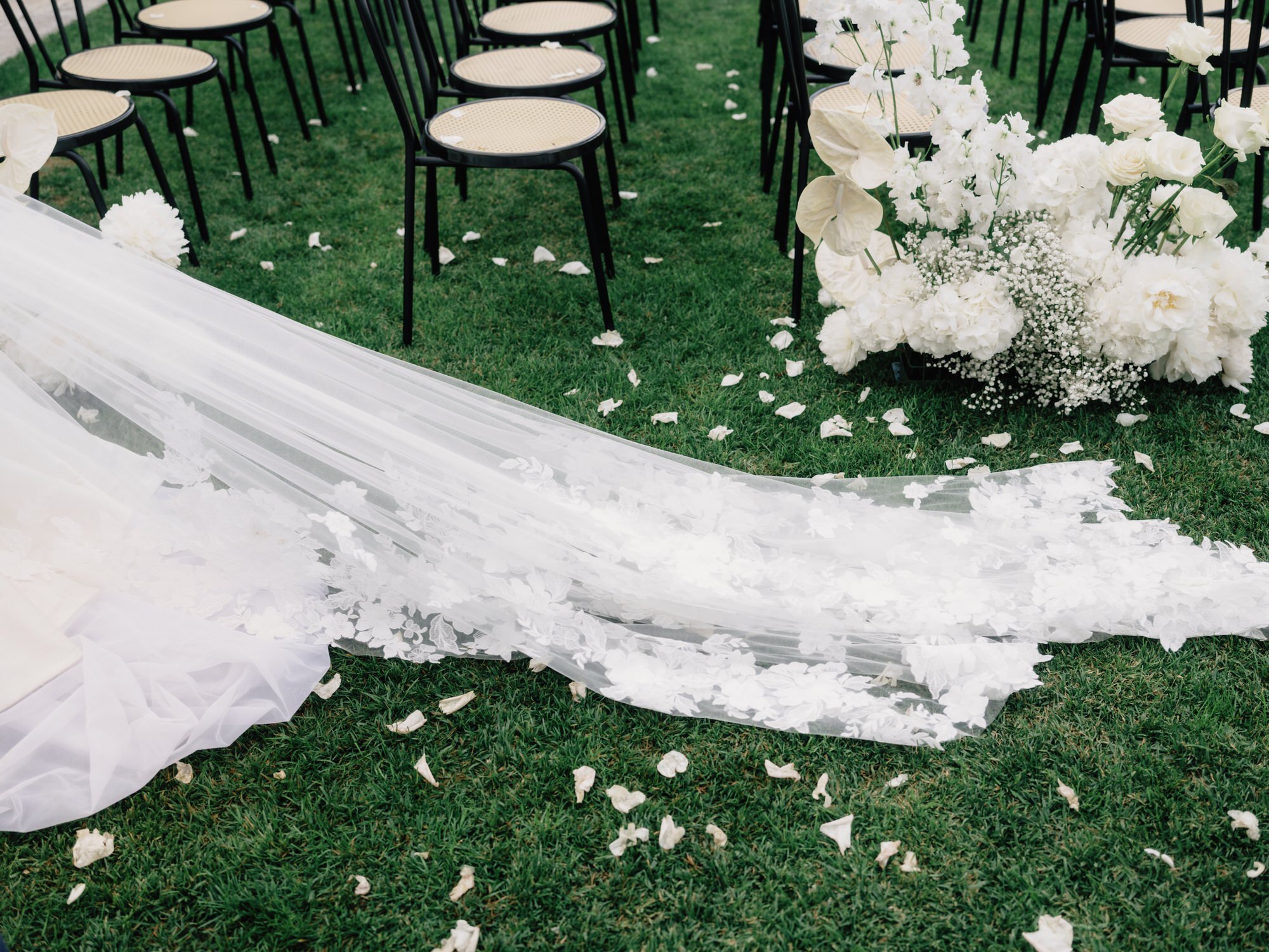 Close-up of the bride’s floral-embroidered veil and scattered petals on the grass after the ceremony at Caruso, A Belmond Hotel in Ravello, Italy, photographed by Jenny Fu.