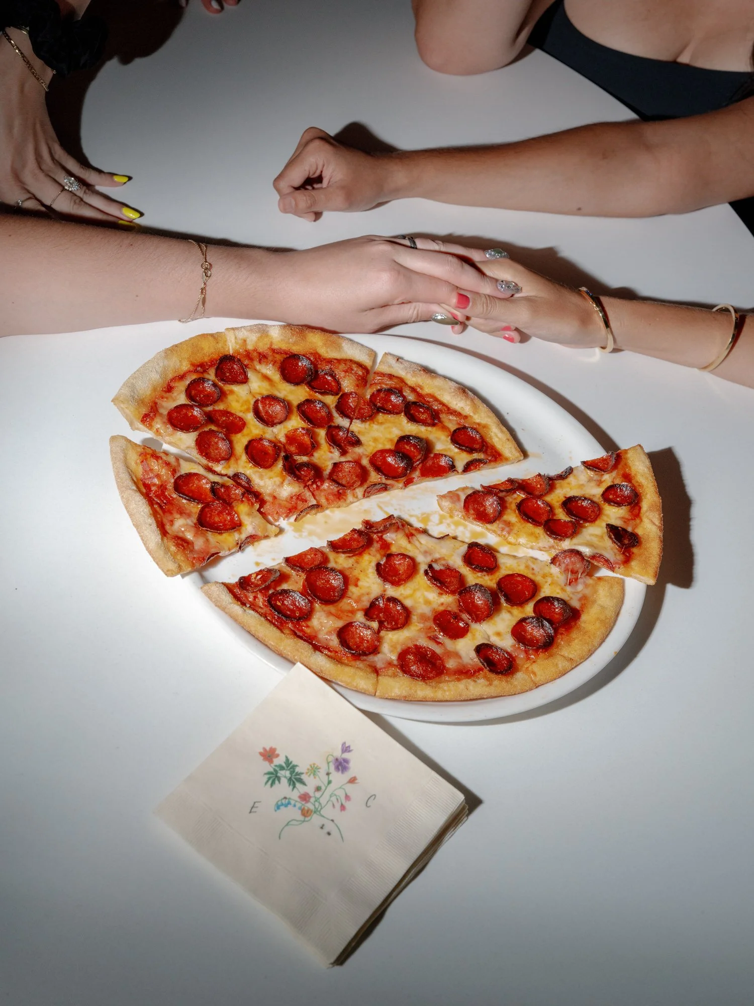 Editorial detail of hands reaching for pepperoni pizza beside a custom monogrammed napkin at Valley Rock Inn in Sloatsburg, photographed by Jenny Fu.