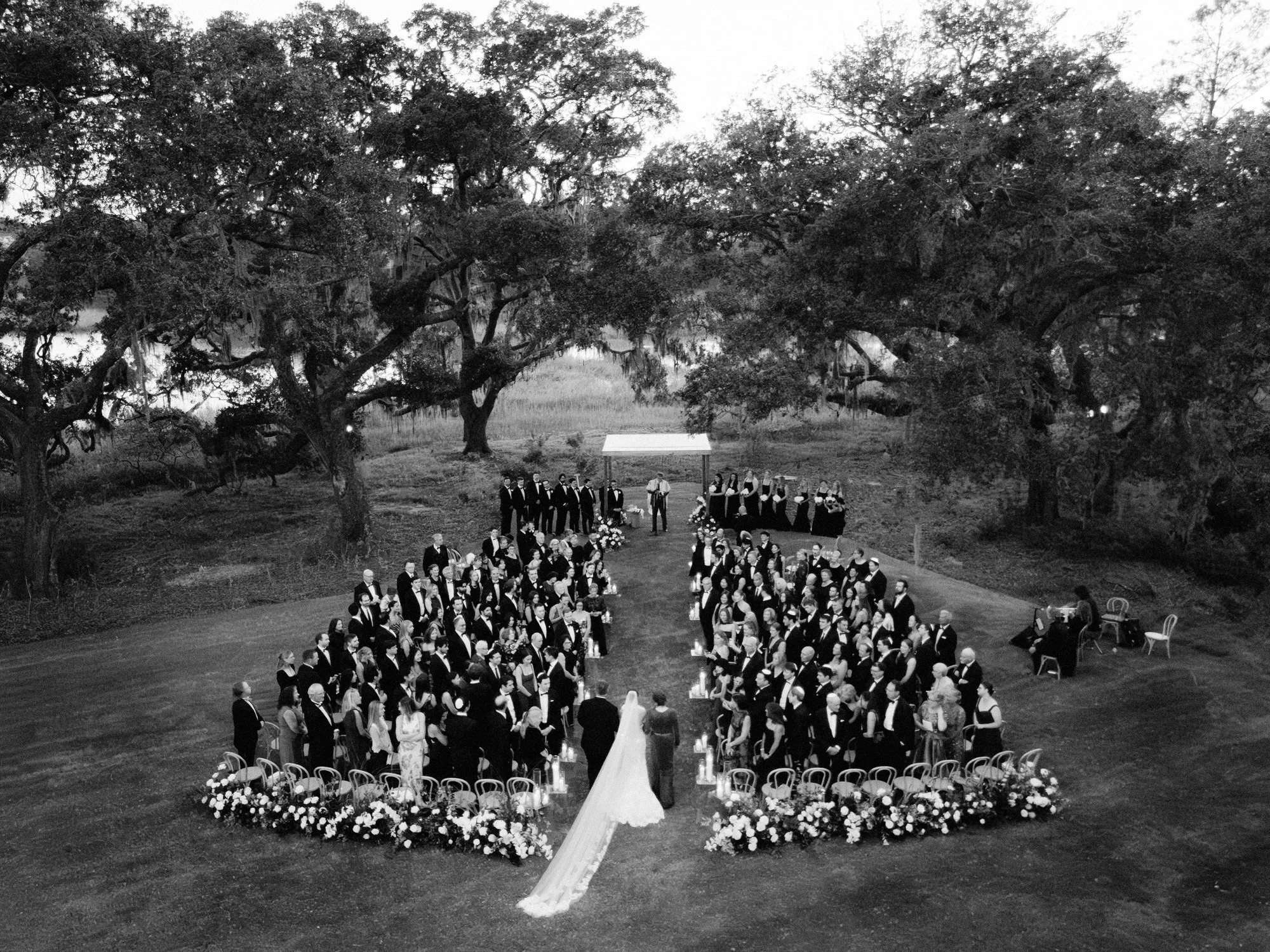 Aerial view of an outdoor wedding ceremony framed by sprawling oak trees at The Dunlin in Okatie, South Carolina, photographed by Jenny Fu.