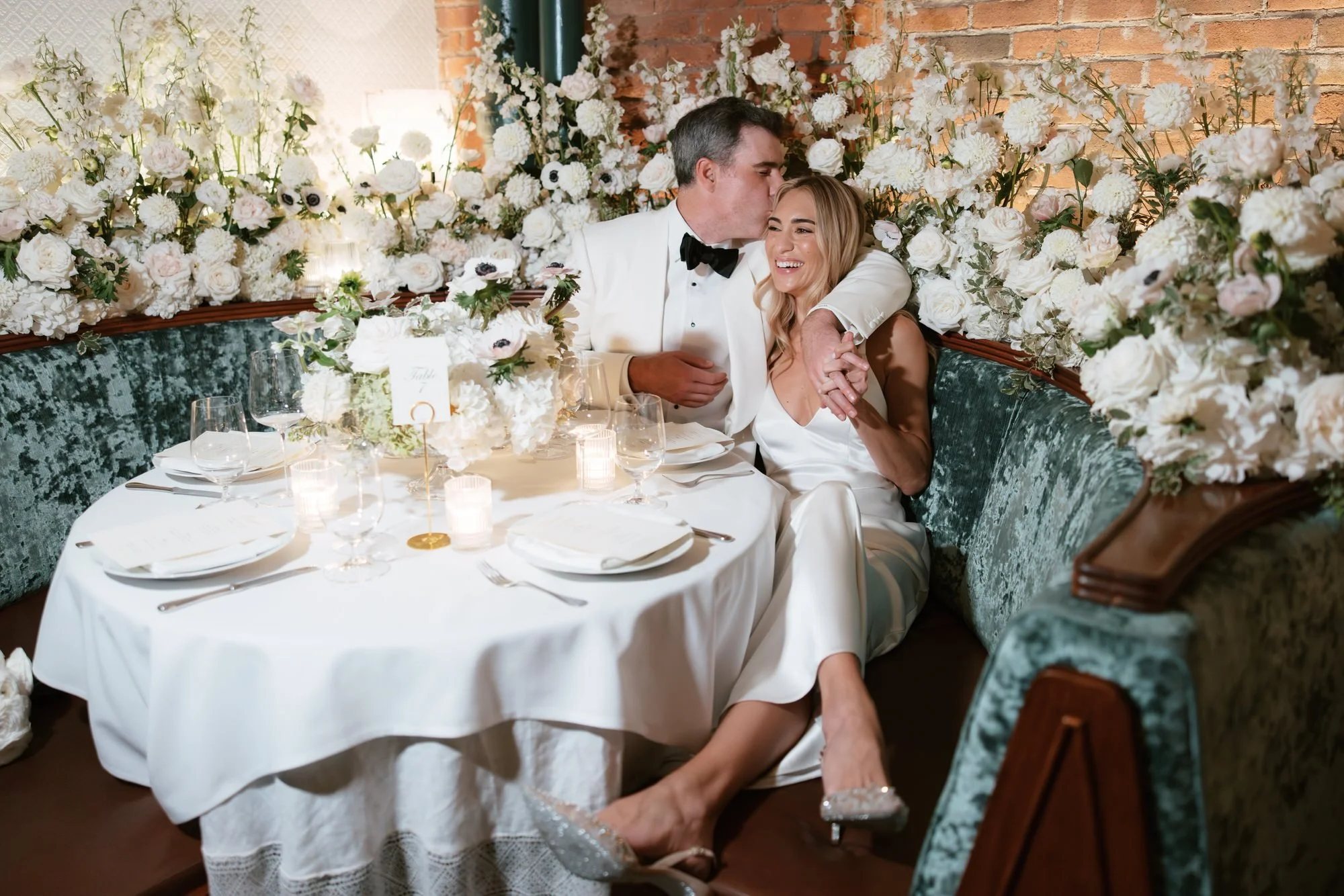 Bride and groom sharing a tender moment at their sweetheart table framed by romantic white florals at Torrisi in Manhattan, photographed by Jenny Fu.