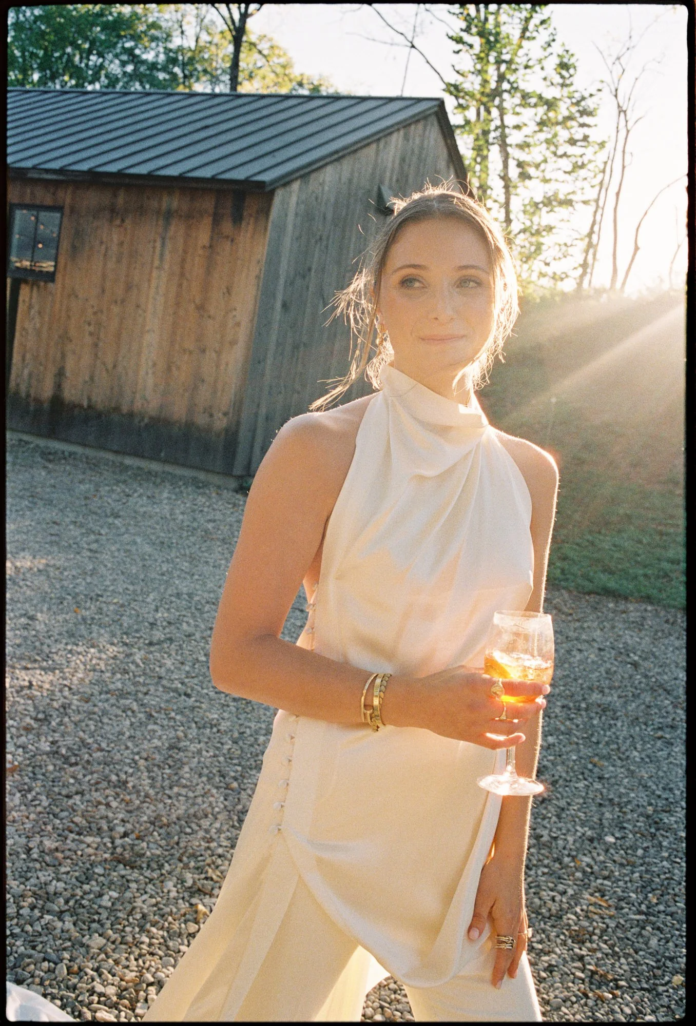 Close-up of bride holding a wine glass, lit by soft sunset light outside the barn at Troutbeck in Amenia, photographed by Jenny Fu.